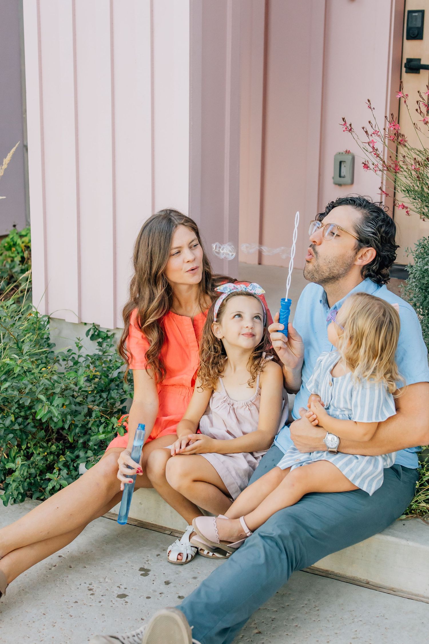 Family blowing bubbles together while sitting on outdoor steps.