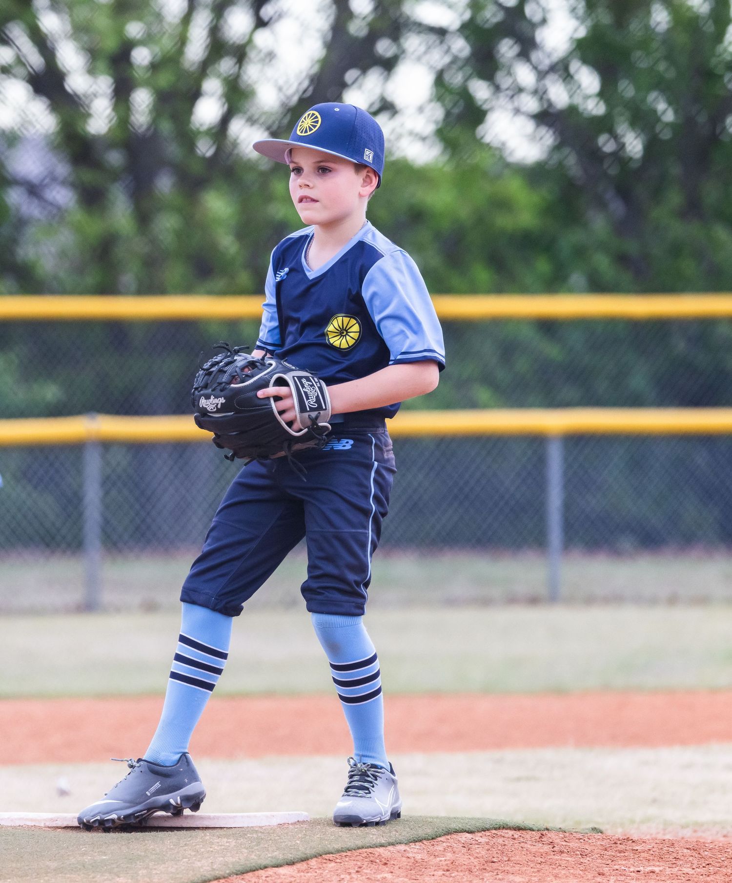 A young baseball pitcher in navy blue uniform stands in pitching position on the mound during a youth league game.