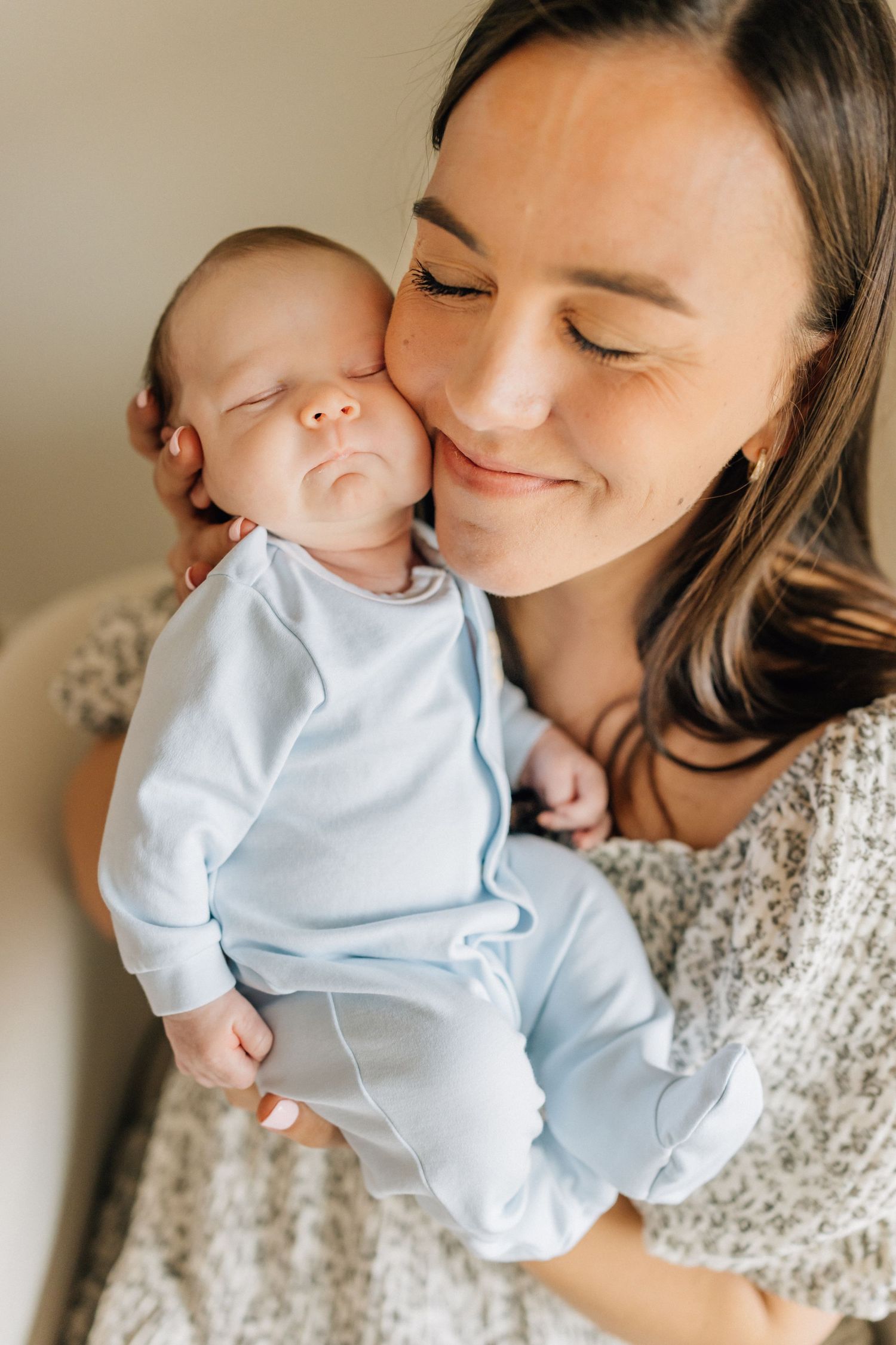 A sleeping baby in light blue sleepwear rests peacefully against an embracing caregiver in a soft knit sweater.
