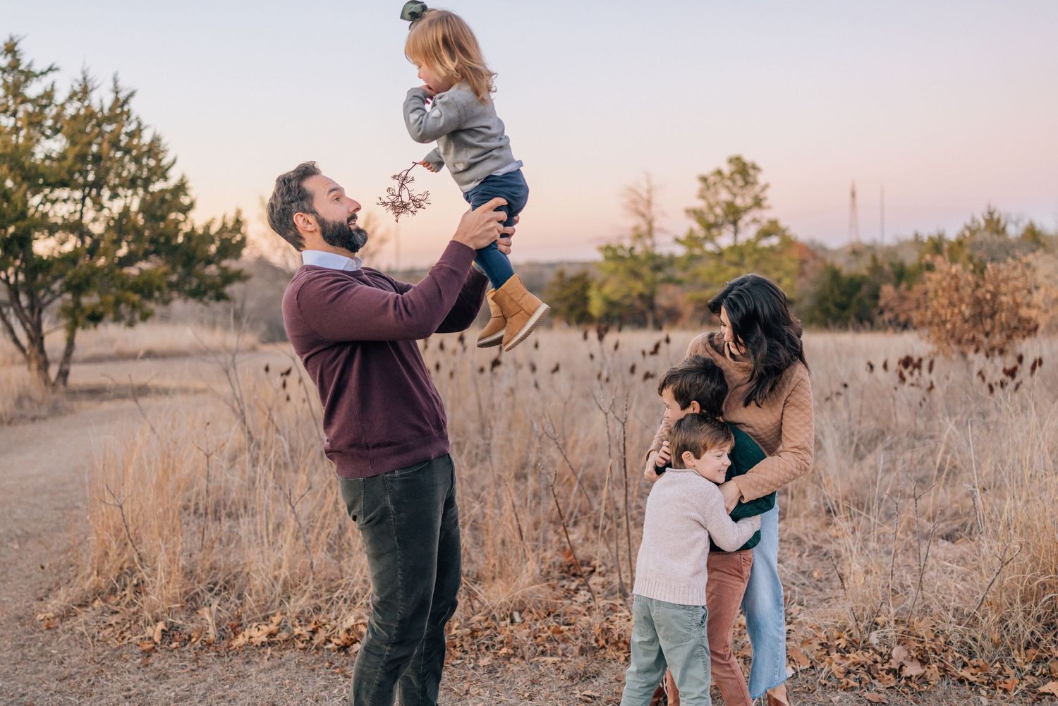 Family enjoying time together outdoors in a golden field during sunset with trees in the background.