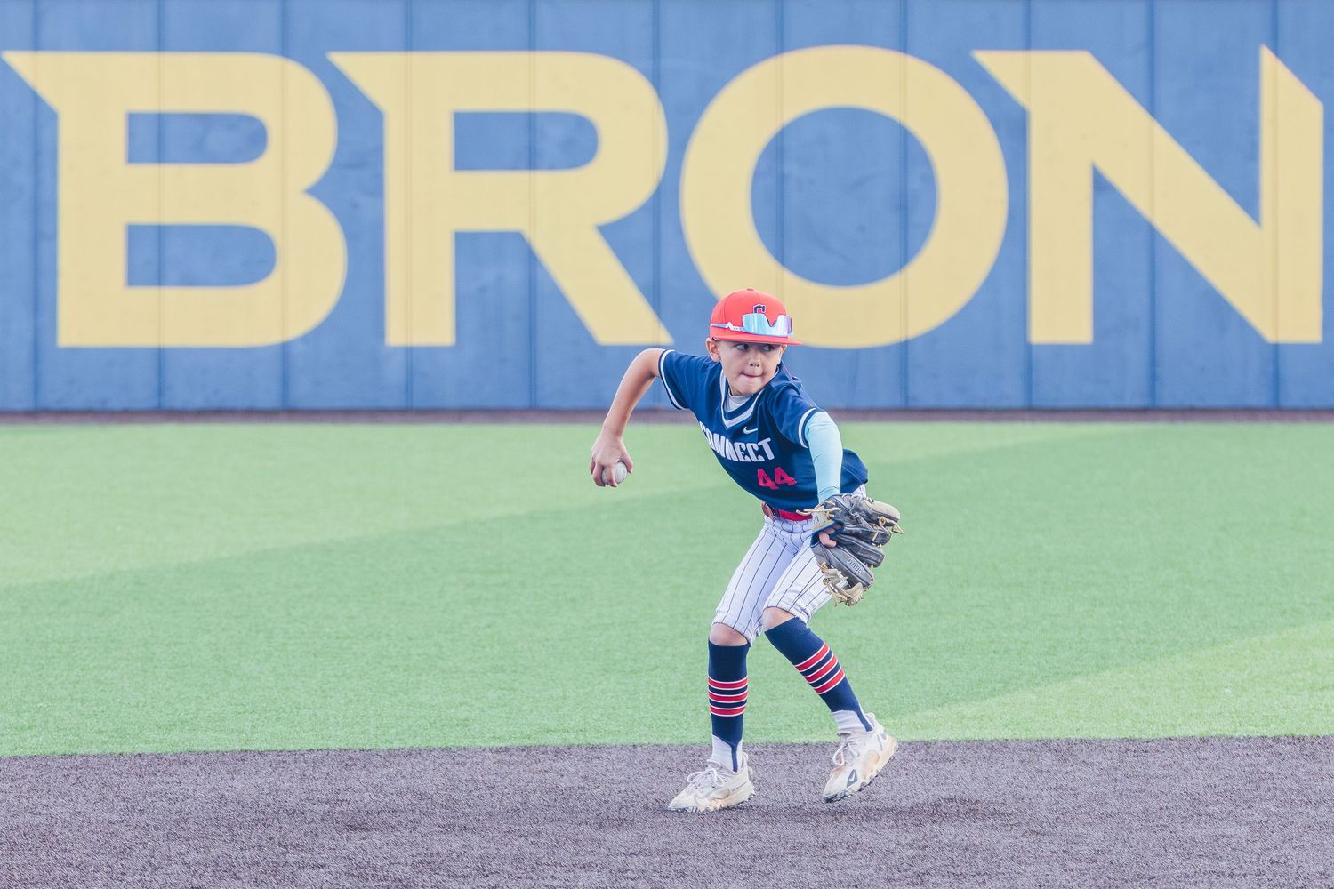 Baseball infielder in blue uniform positions to field a ground ball on artificial turf field with blue wall in background.