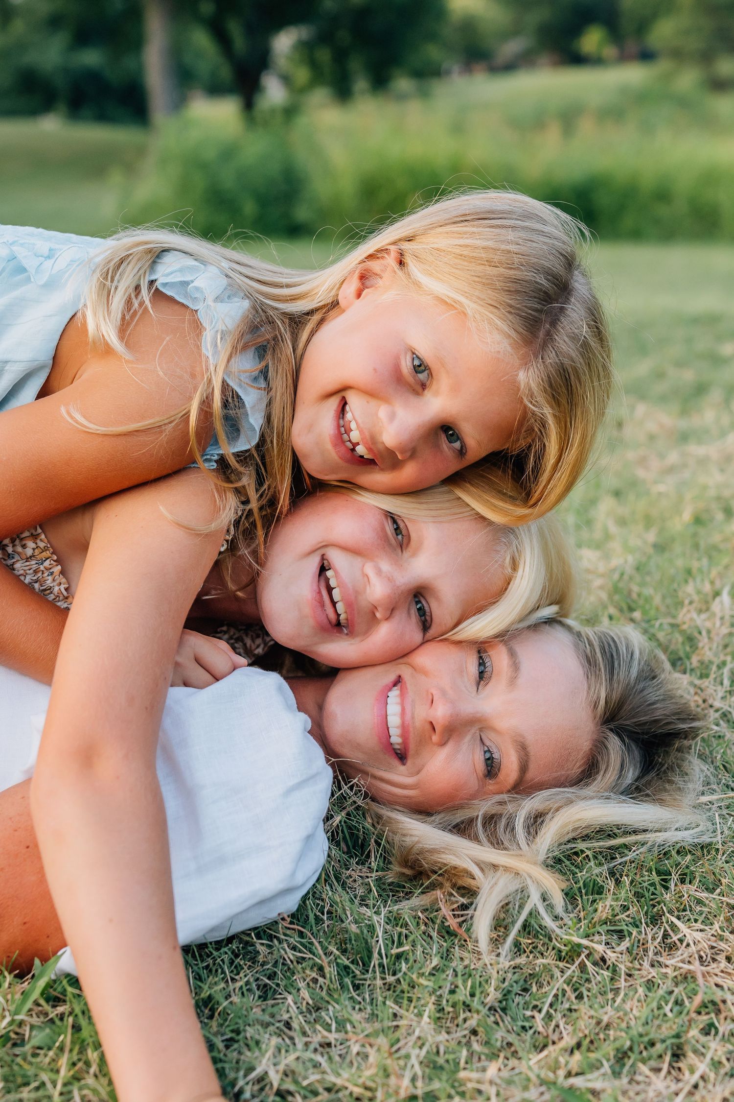 Three people lying in grass outdoors sharing happy smiles together.