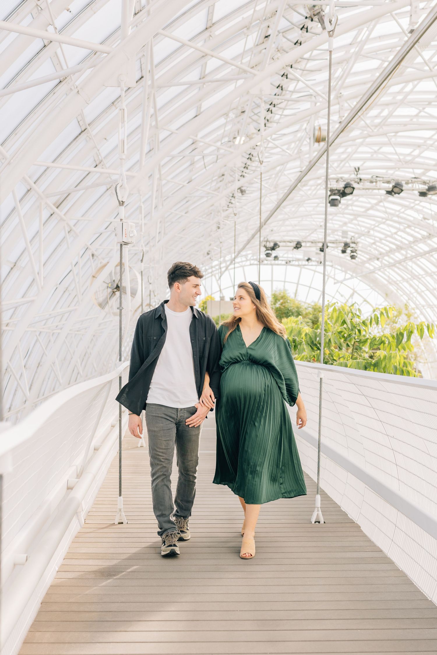 Couple walking through white covered walkway with greenery visible through lattice roof.