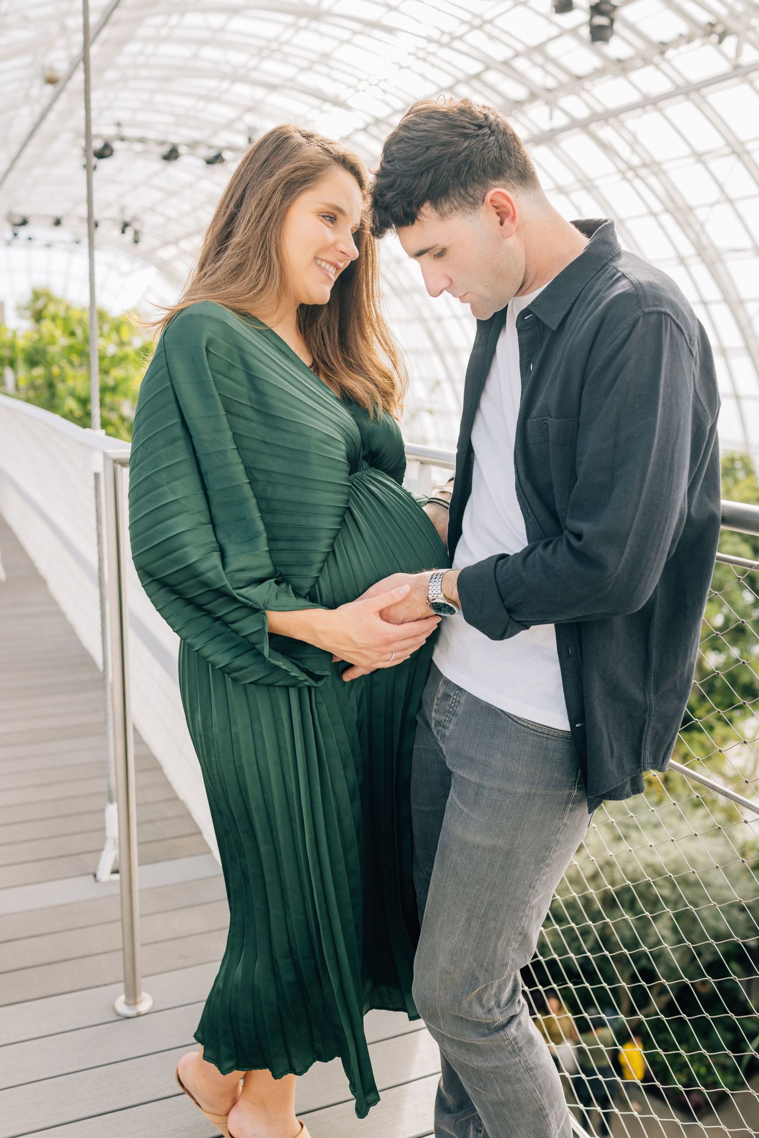 Couple sharing tender moment while expecting in a greenhouse setting.