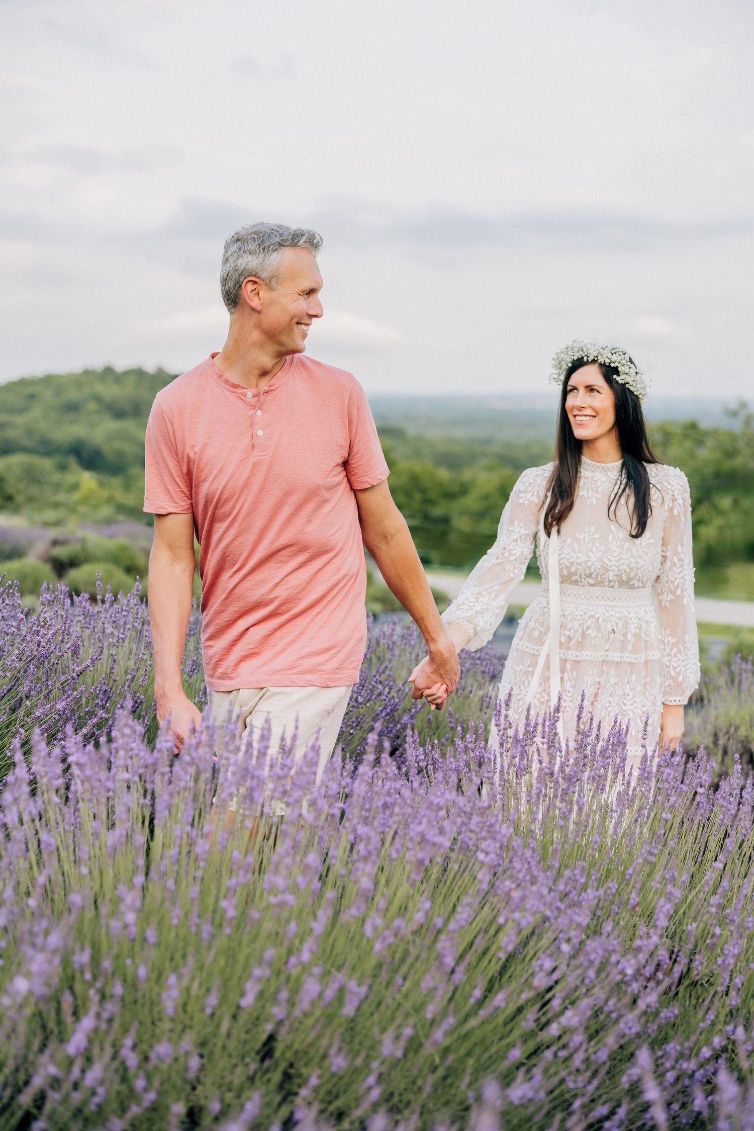 Couple holding hands while walking through a blooming purple lavender field on a misty summer day.