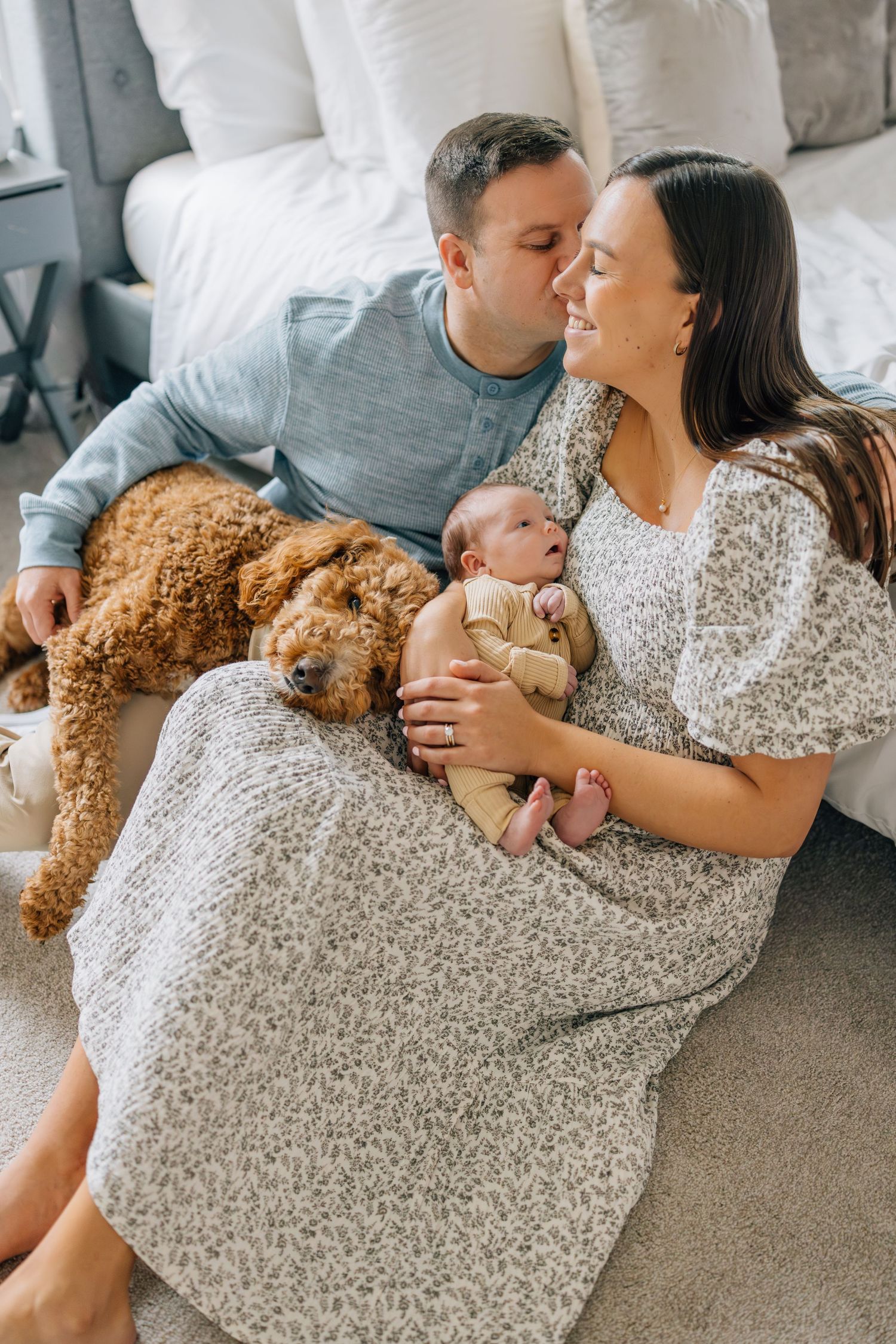 Couple relaxing on couch with newborn baby and teddy bear.