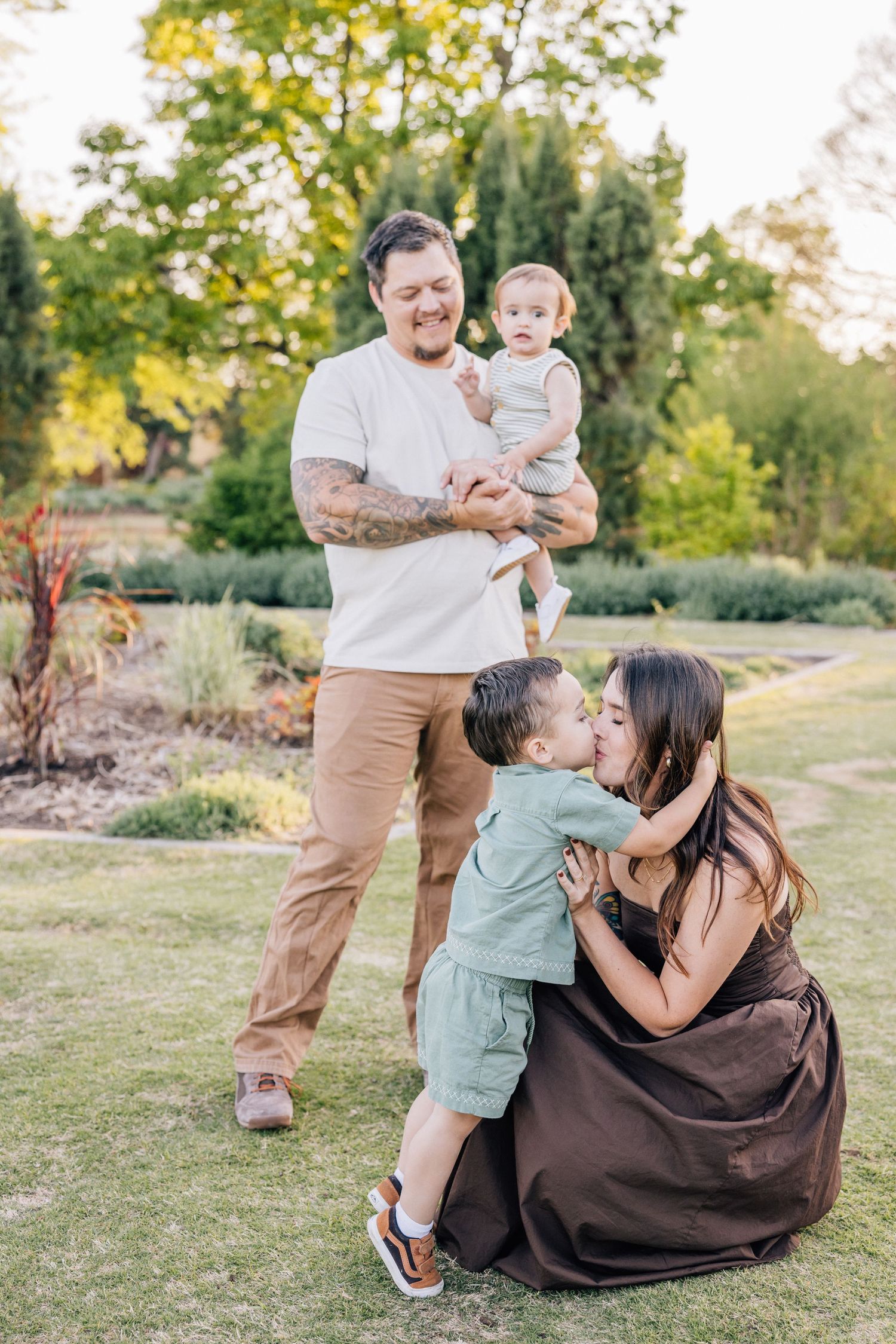 Outdoor family portrait in a garden setting with sunlit greenery and natural landscaping in the background.