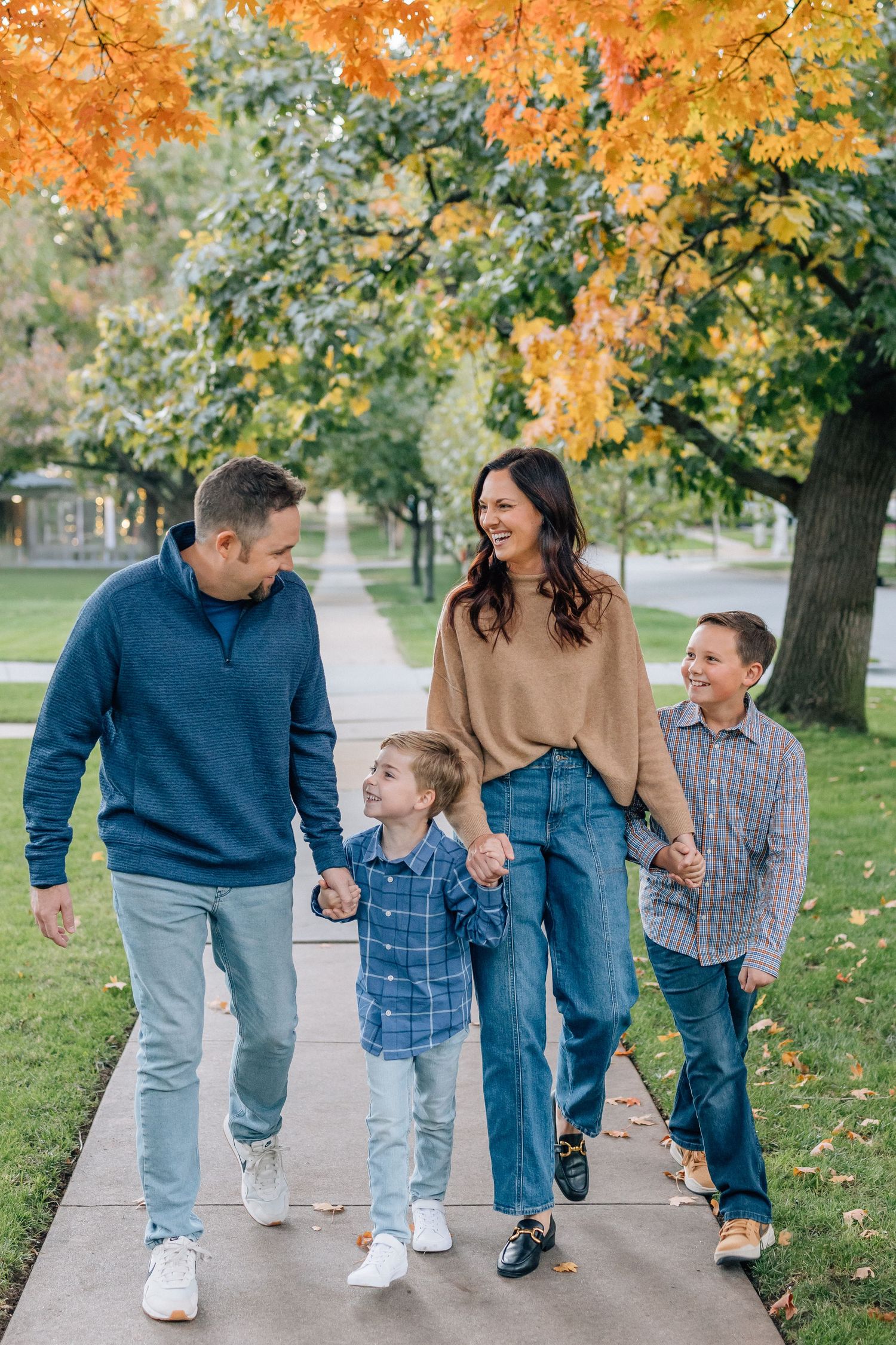 Family walking together on autumn sidewalk under colorful fall foliage.