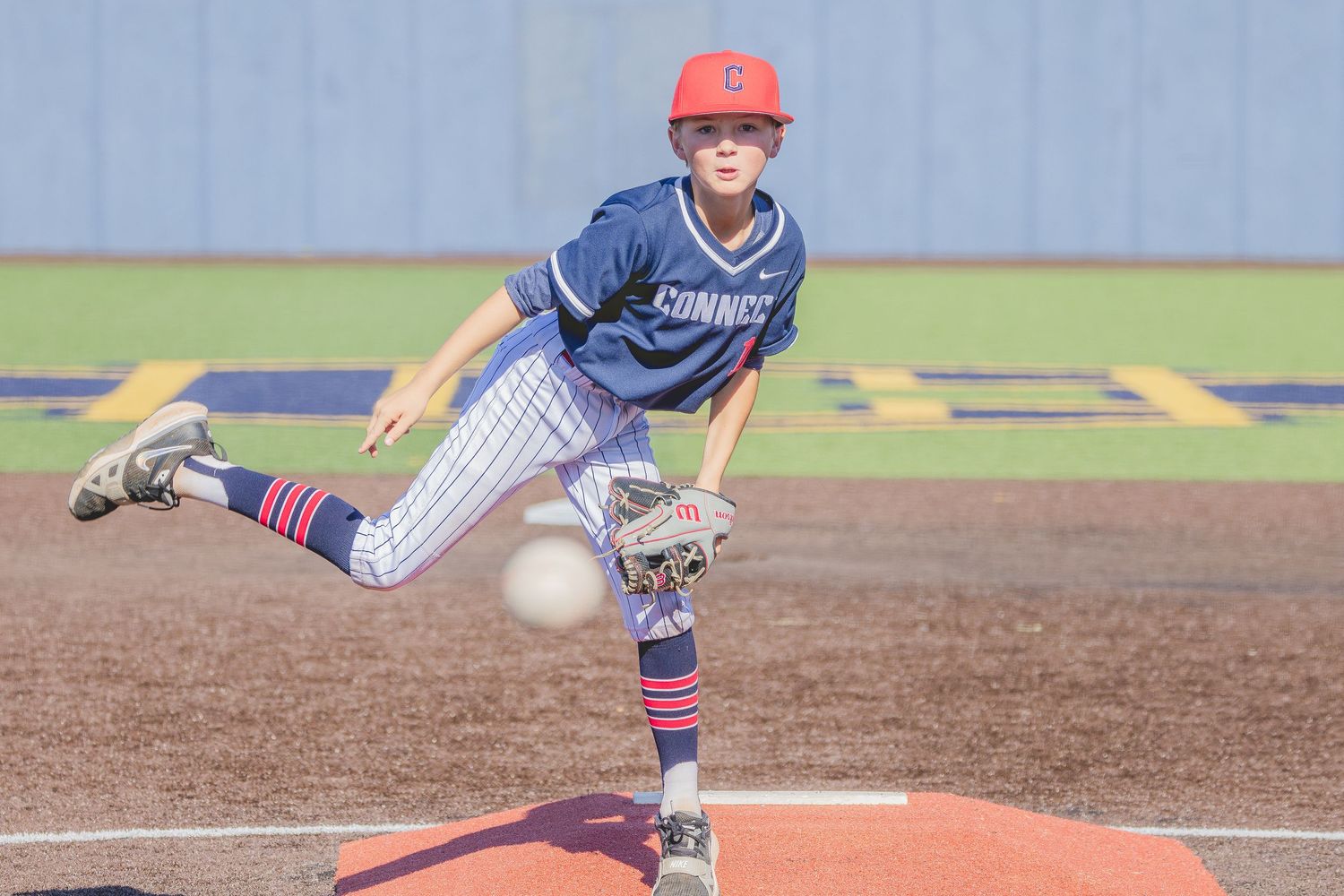 Baseball pitcher in blue striped uniform and red cap follows through on mound during game.