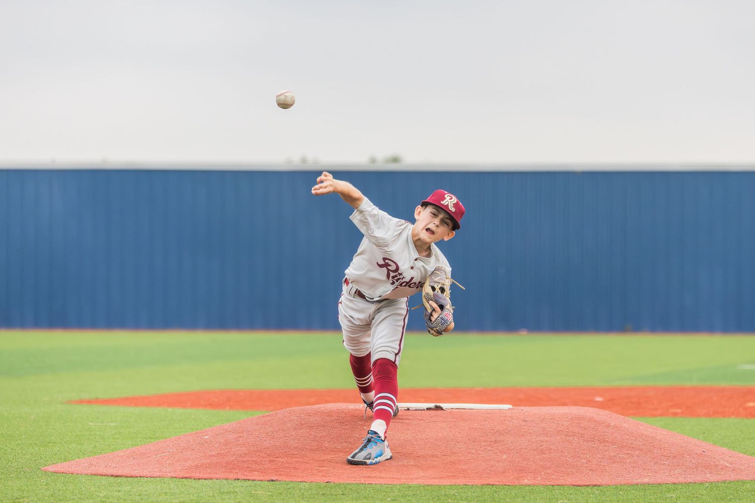 Baseball pitcher in red uniform stands on mound during game delivering pitch with intense focus and form.