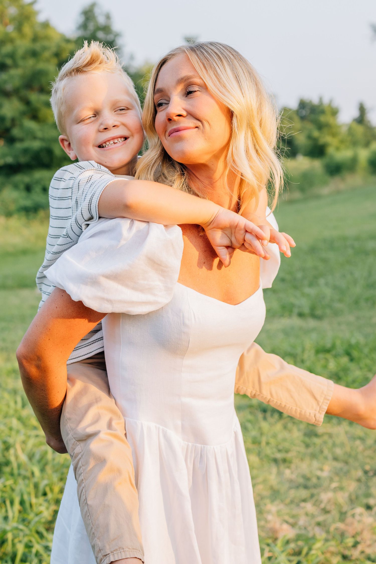 A joyful outdoor moment shared between parent and child in a sunny meadow with greenery in the background.