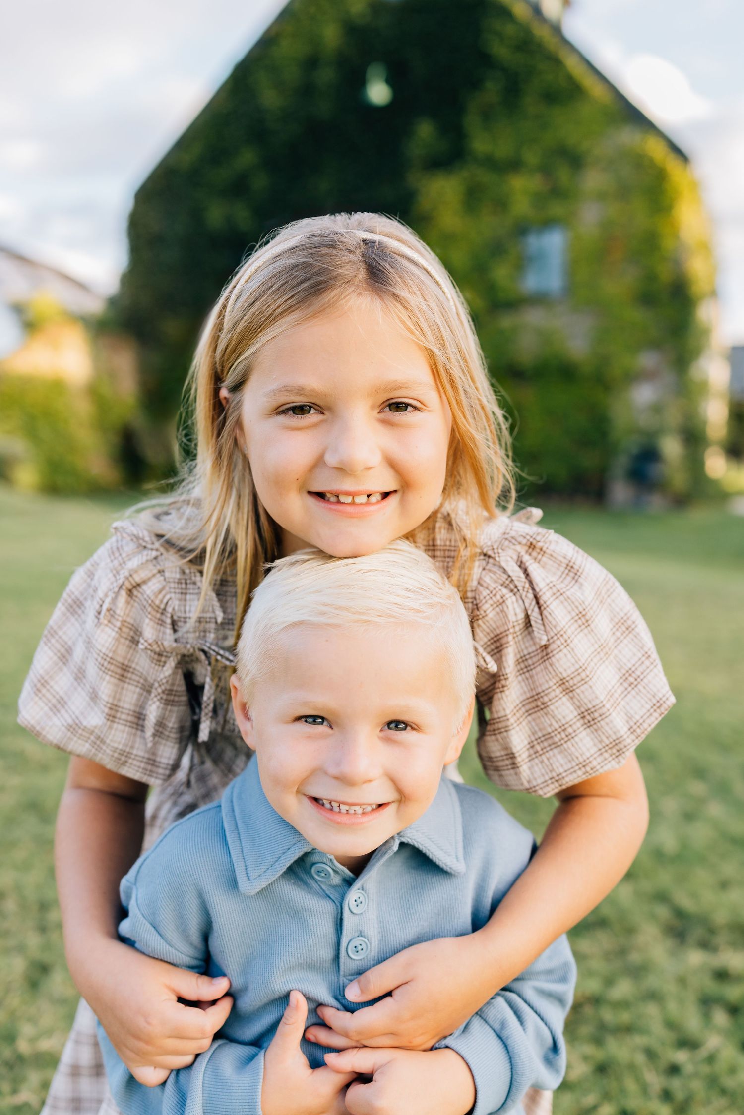 Two children share a happy moment together outdoors on a sunny day with a house in the background.