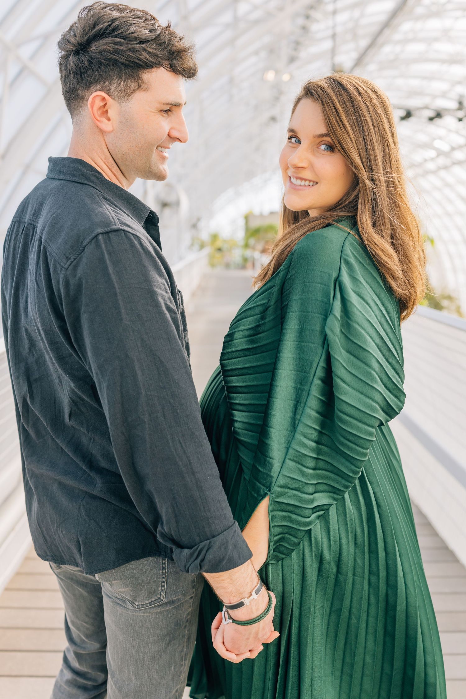 A couple in casual attire sharing an intimate moment on a covered walkway, with a green pleated dress as a focal point.