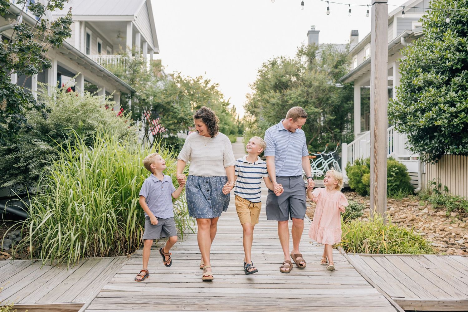Group of people walking together on a wooden boardwalk surrounded by lush greenery on a sunny day.