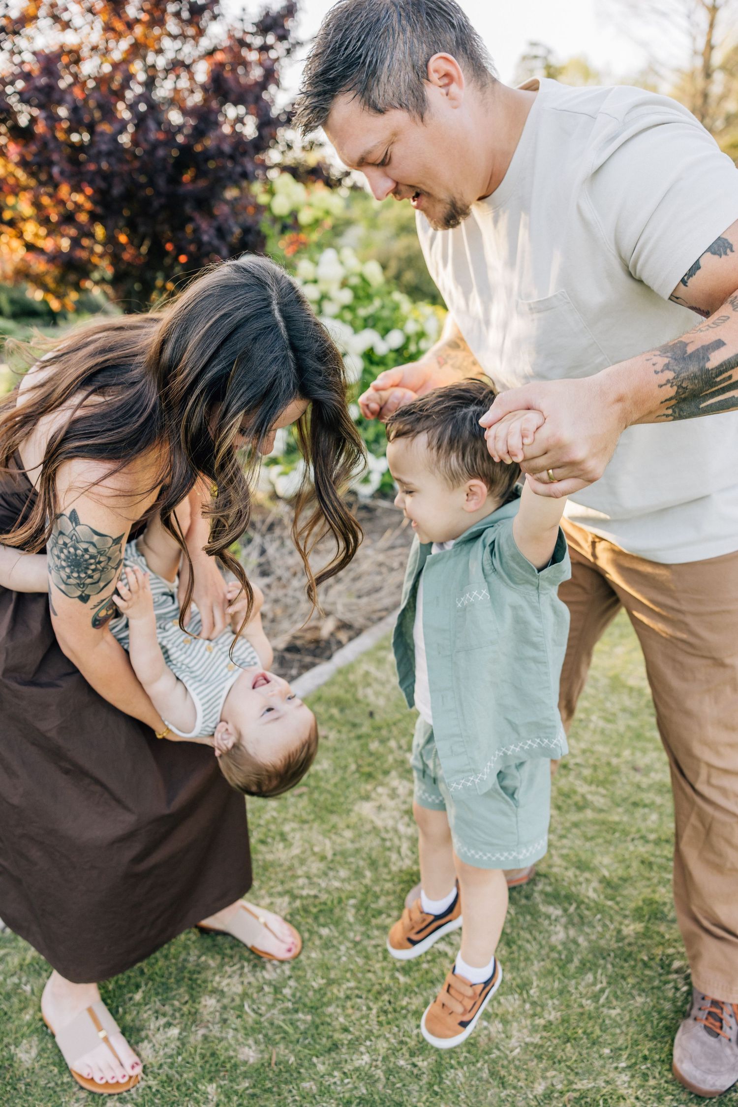 A family shares a playful moment together on a grassy lawn with autumn foliage in the background.