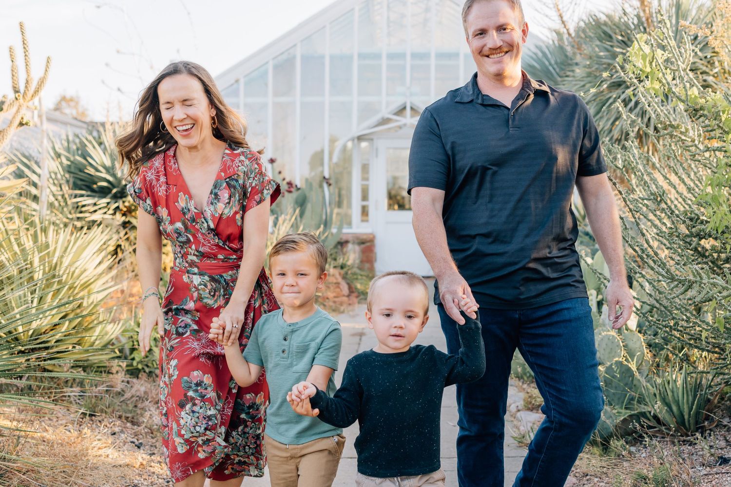 Family wearing colorful outfits poses together in front of desert plants and greenhouse structure.