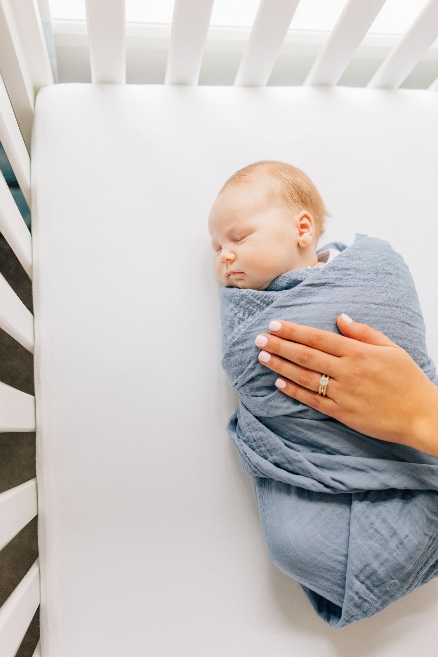 Sleeping newborn swaddled in blue blanket in white crib.