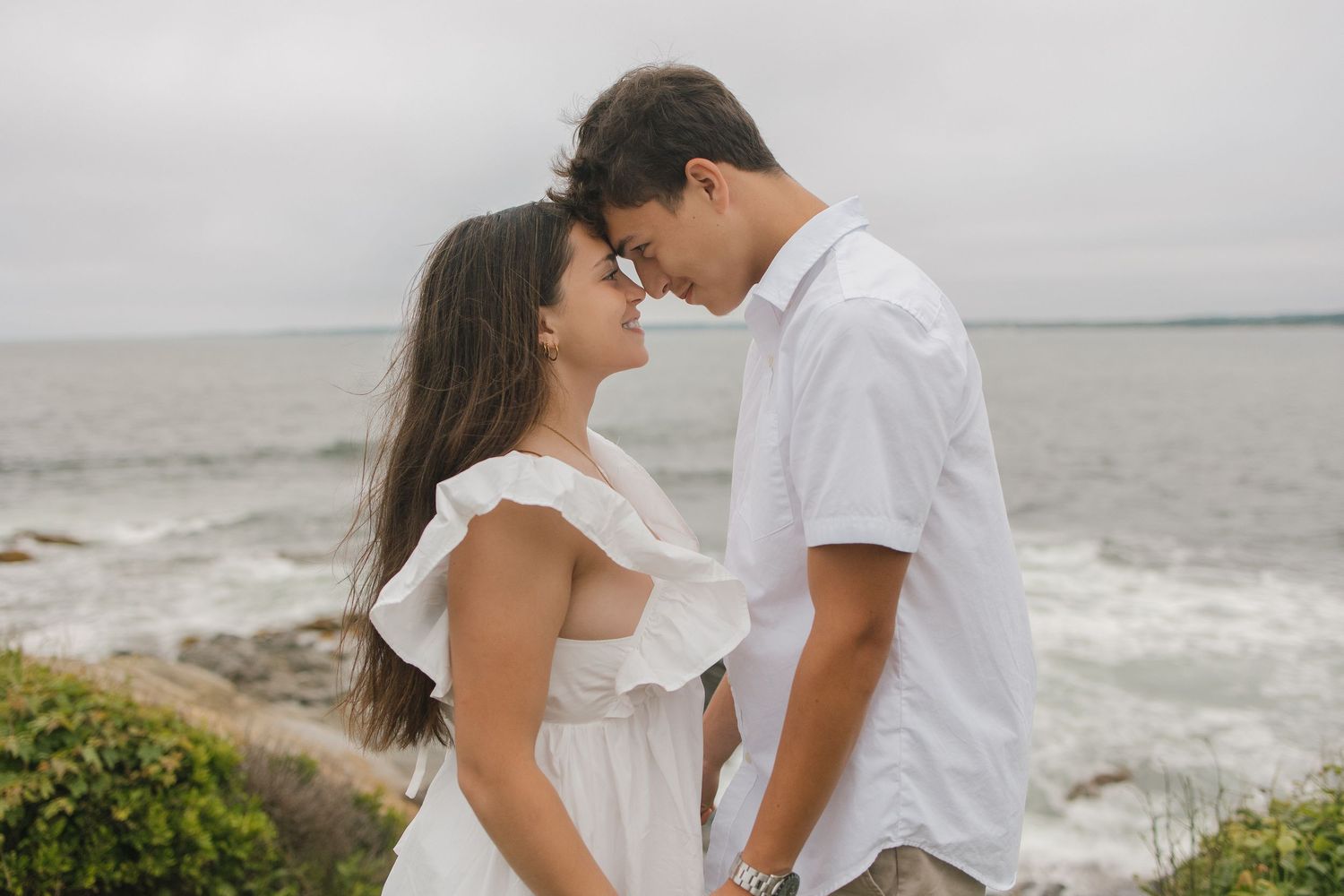 Couple dressed in white sharing tender moments along a dramatic rocky coastline.