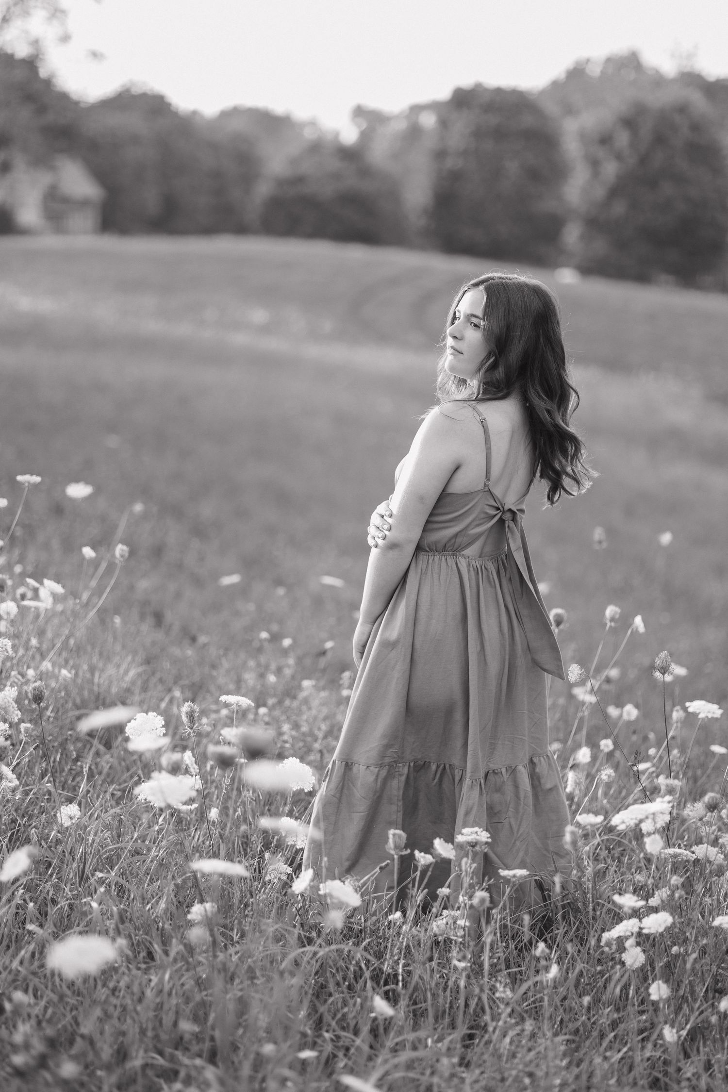 Black and white photo of person in flowing dress standing in field of wildflowers on a summer day.