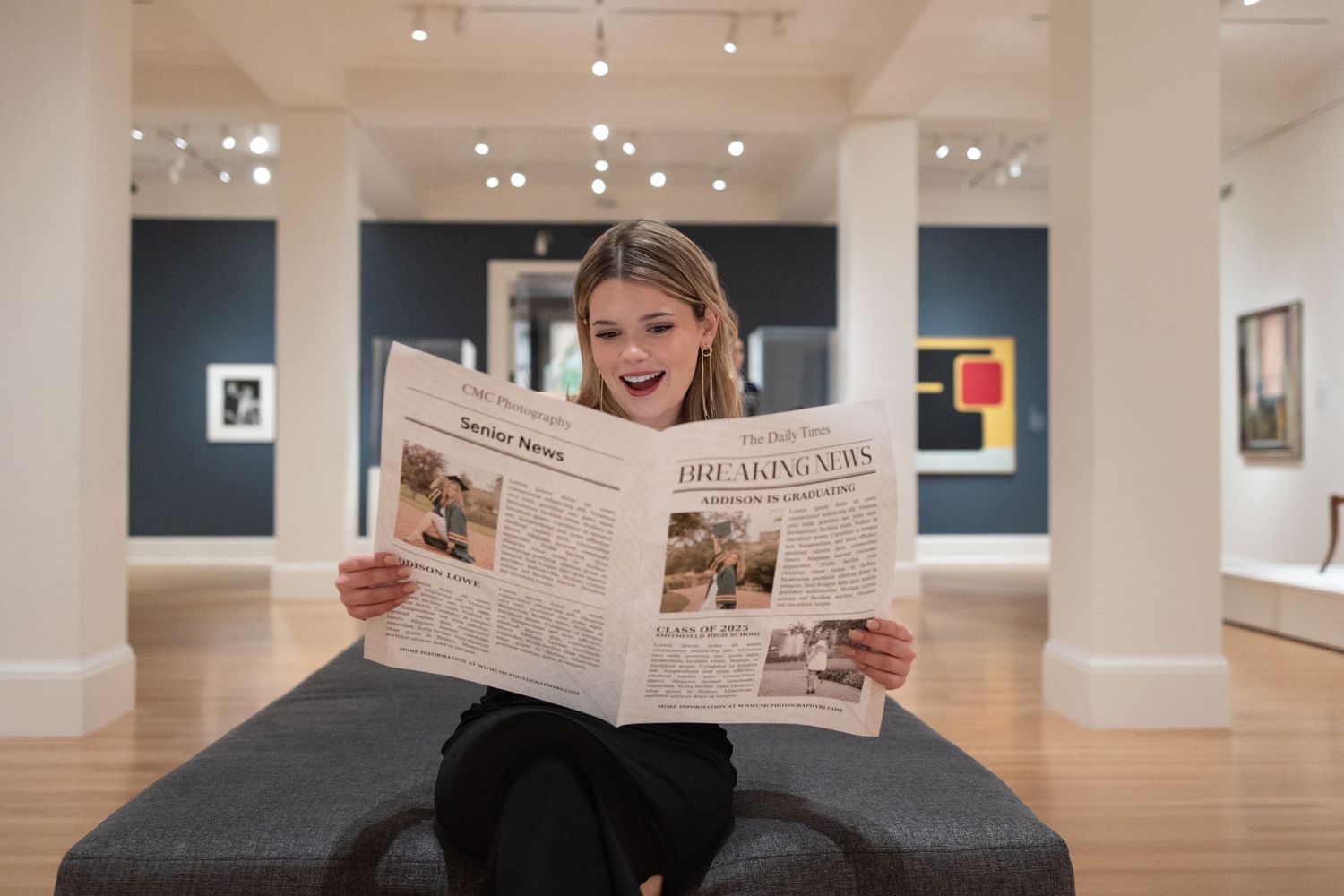 Woman engages with newspaper while sitting on dark bench in gallery space.