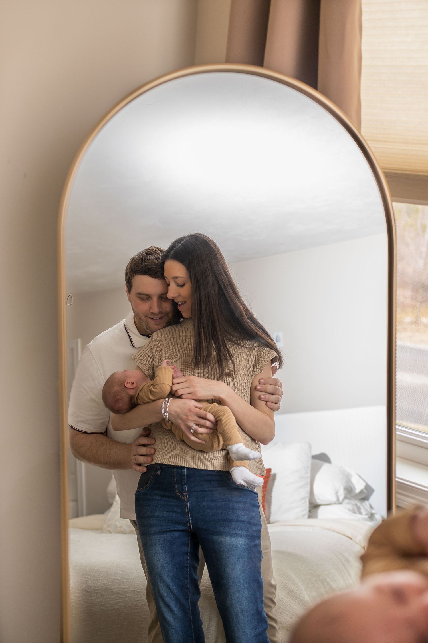 Mirror reflection captures family moment with newborn in bedroom setting.