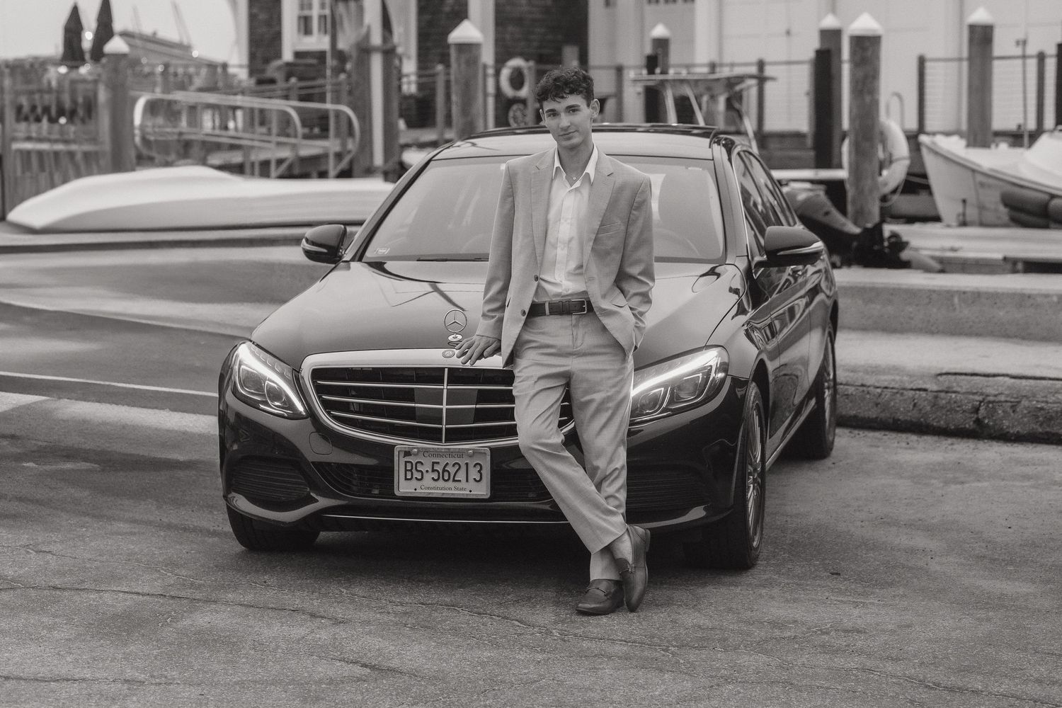 Black and white photo series showing a person standing next to various luxury cars on a street.