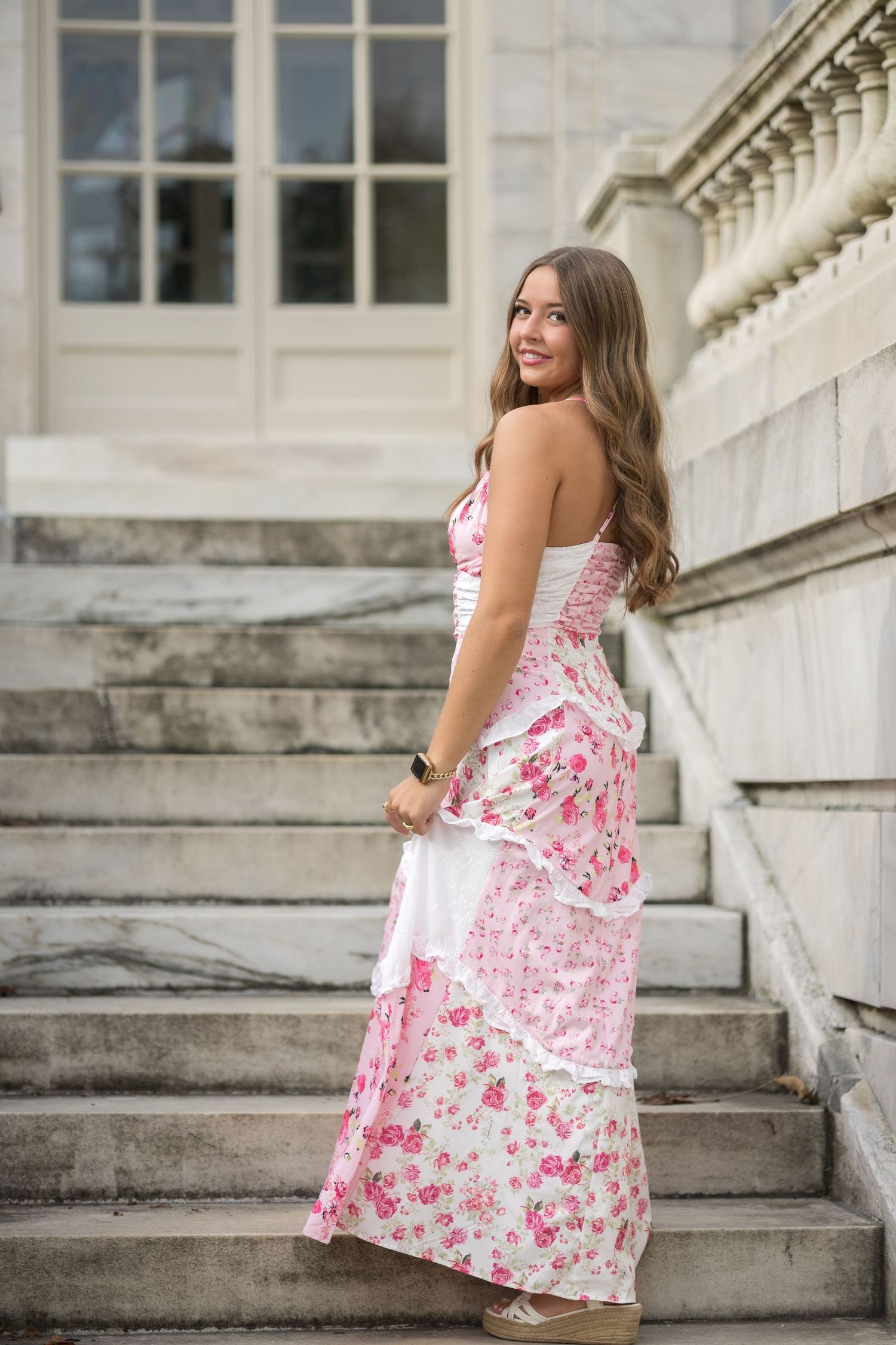 A summery pink and white floral dress is showcased on stone steps of a grand building.
