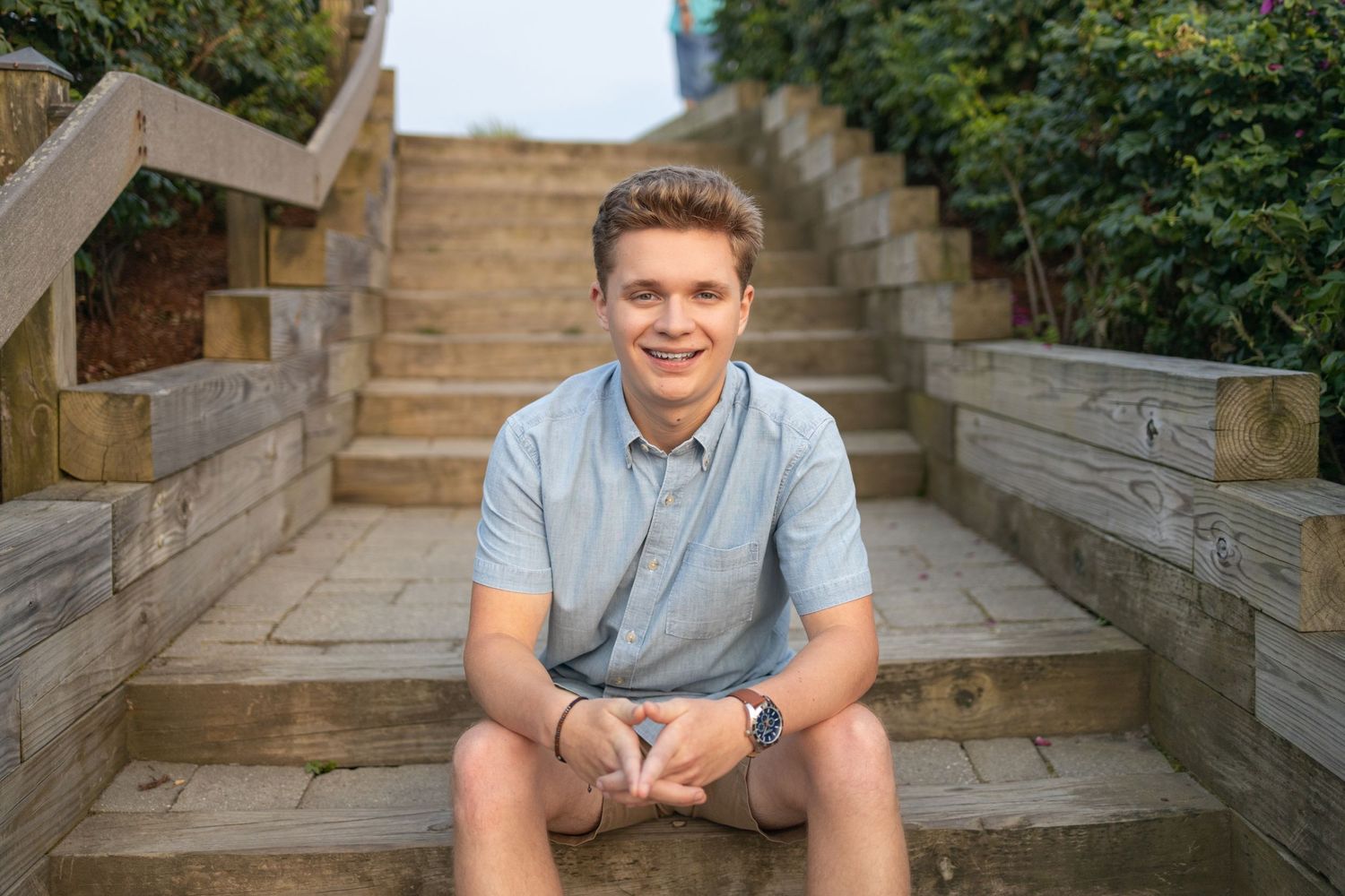 Someone sits on stone steps surrounded by green foliage.