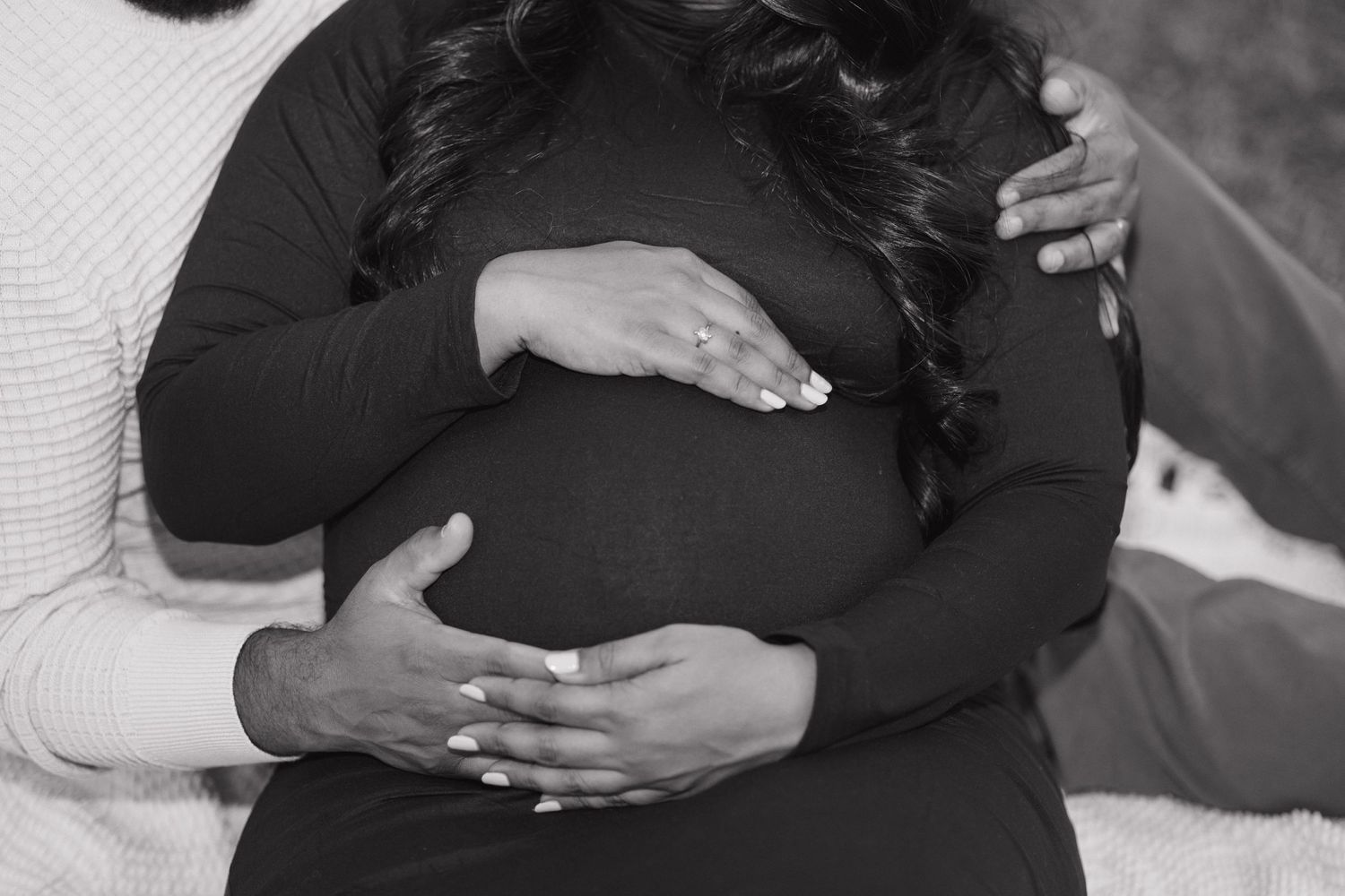 Black and white intimate maternity photo showing hands cradling baby bump.