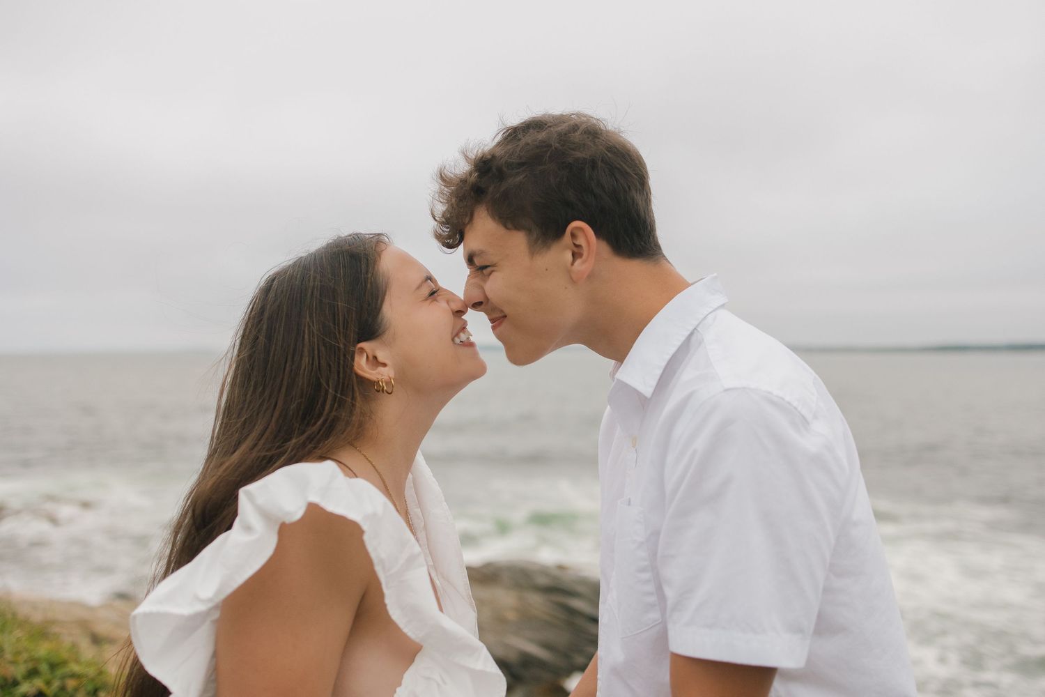 Intimate couple in matching white outfits pose together against a misty ocean backdrop.