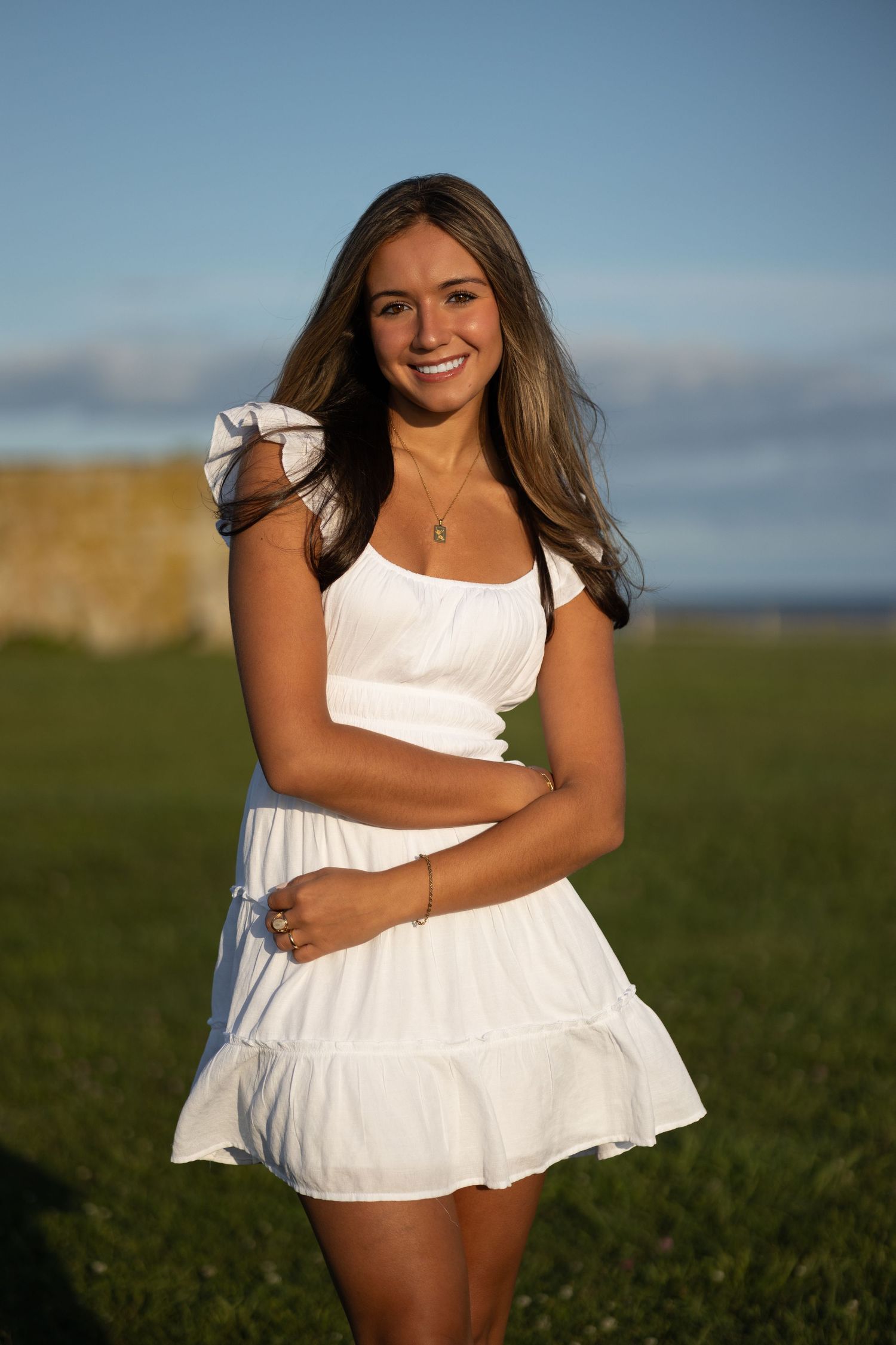 Woman wearing white sundress poses in open field during golden hour photo session.