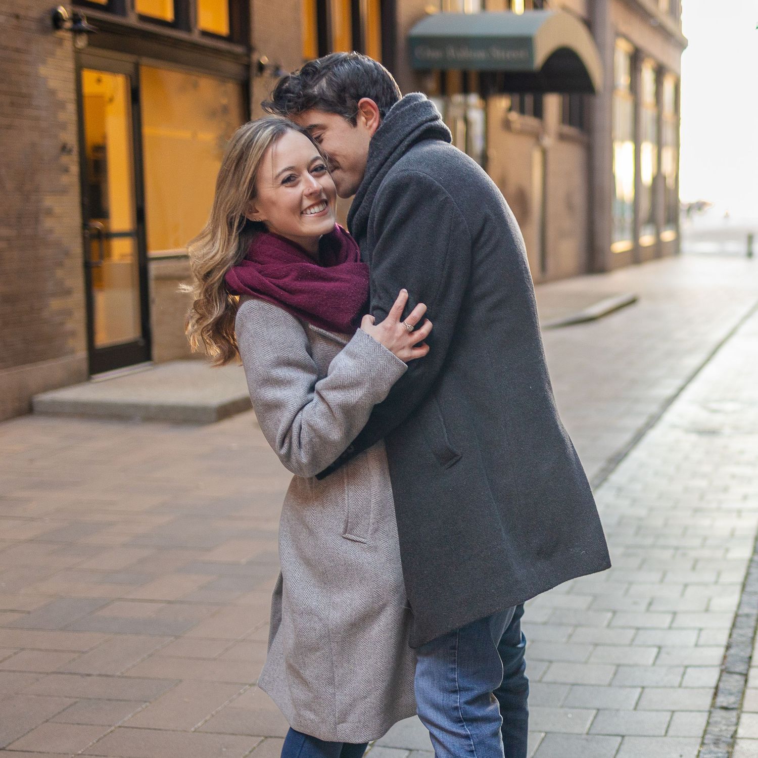 A romantic moment between a couple embracing on a city street at dusk.