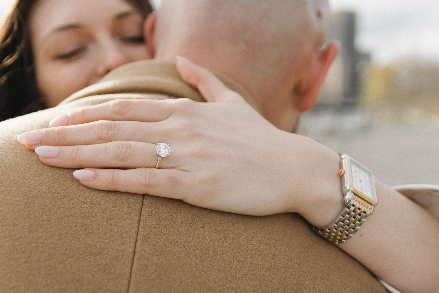 A close-up shot showing hands embracing with a diamond ring and watch visible.