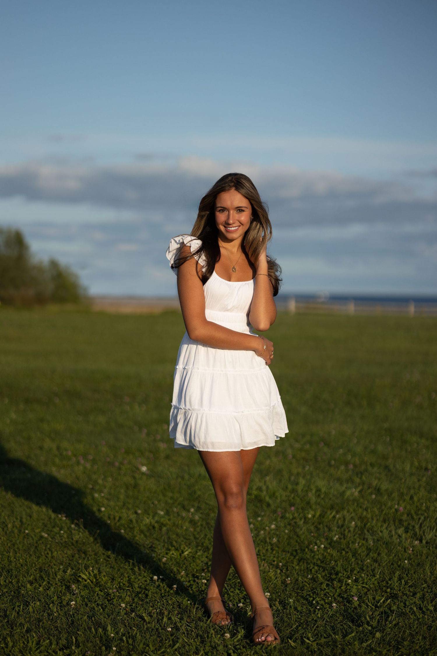 A white summer dress is worn while standing in a grassy field against a blue sky at sunset.