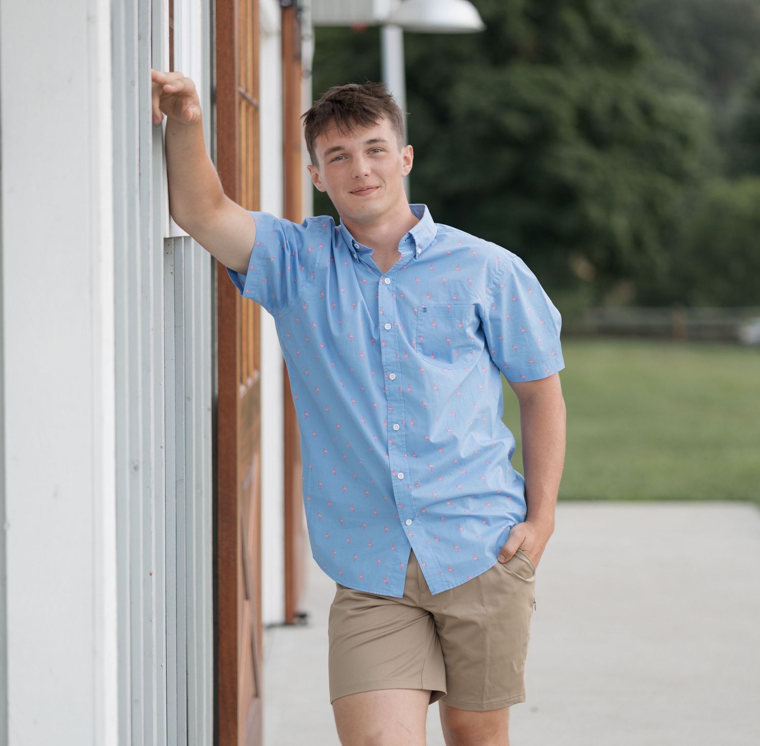 Person in light blue button-down shirt and khaki shorts leaning against white building exterior.