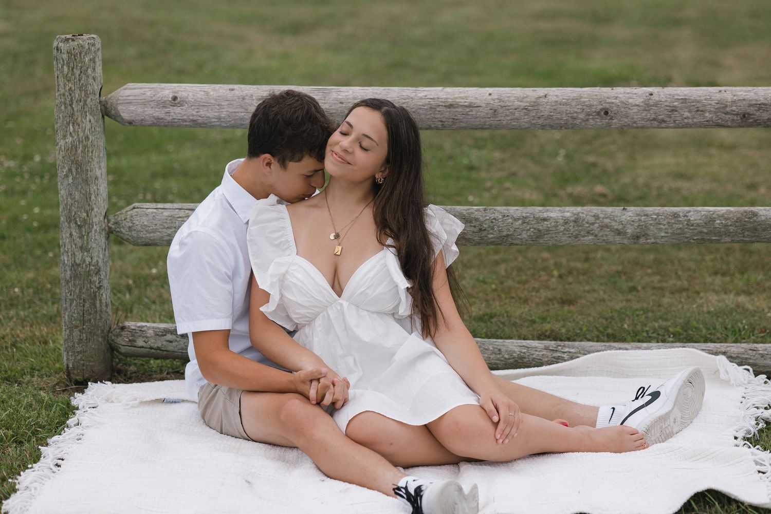 A couple in white outfits shares an intimate moment while reclining on a blanket outdoors.