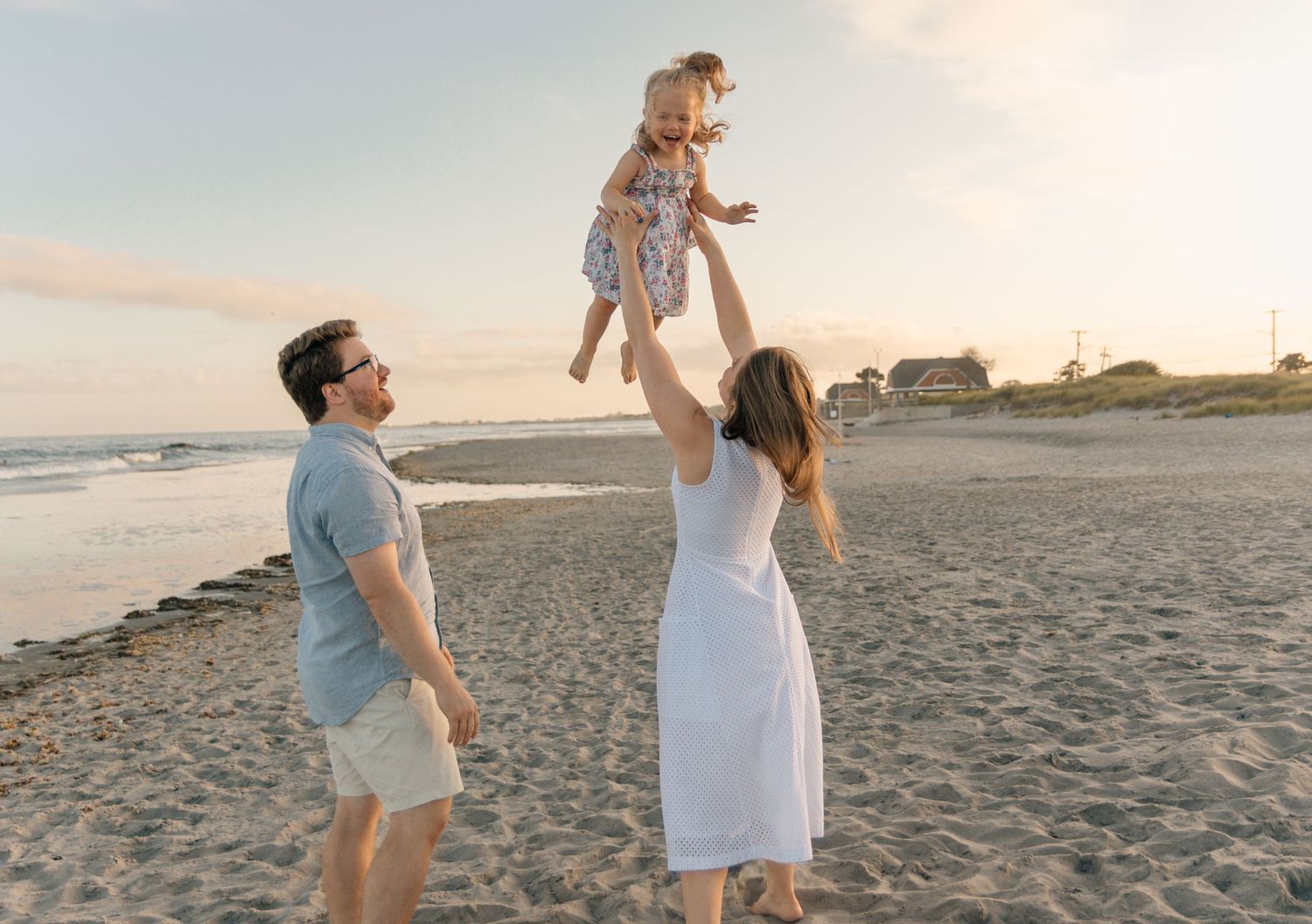 A happy family plays together on the beach at sunset, lifting their child in the air.