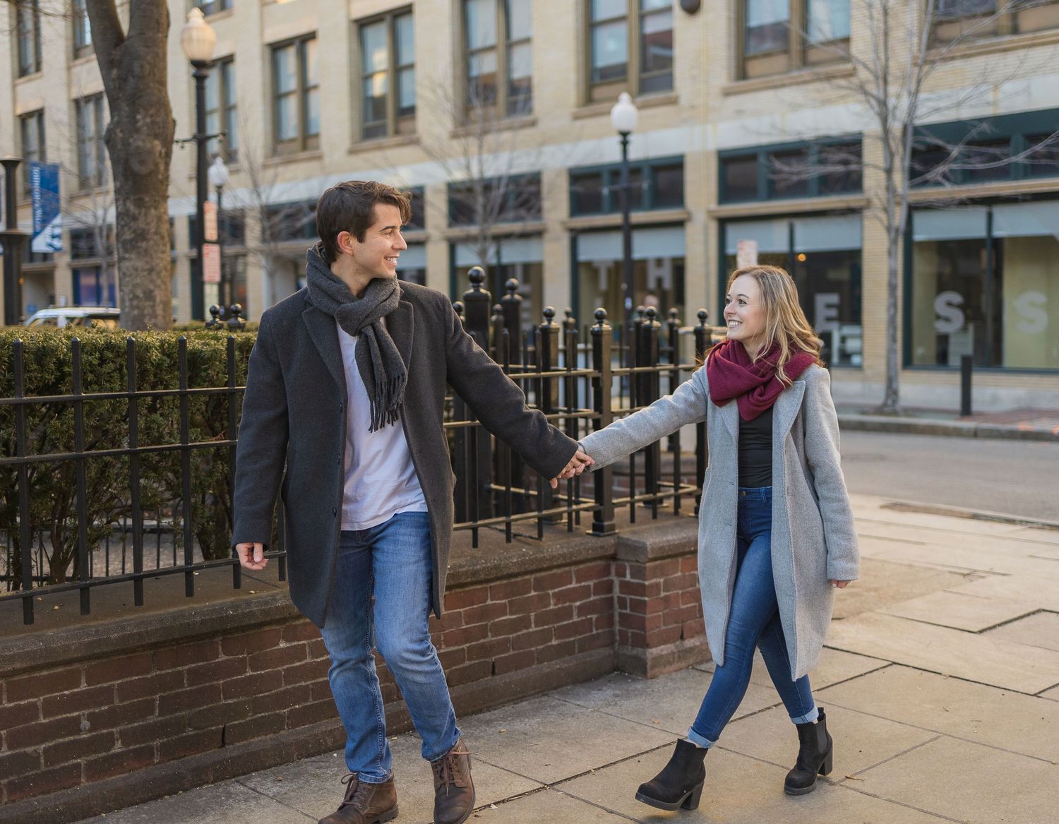 A playful couple holding hands while walking along a city street.