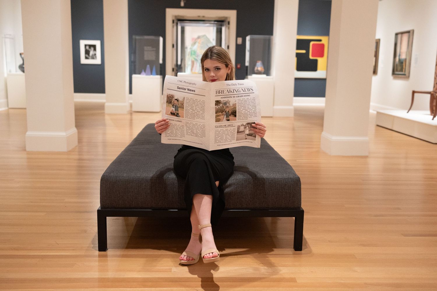 Person relaxes on bench while reading newspaper in art gallery with hardwood floors.