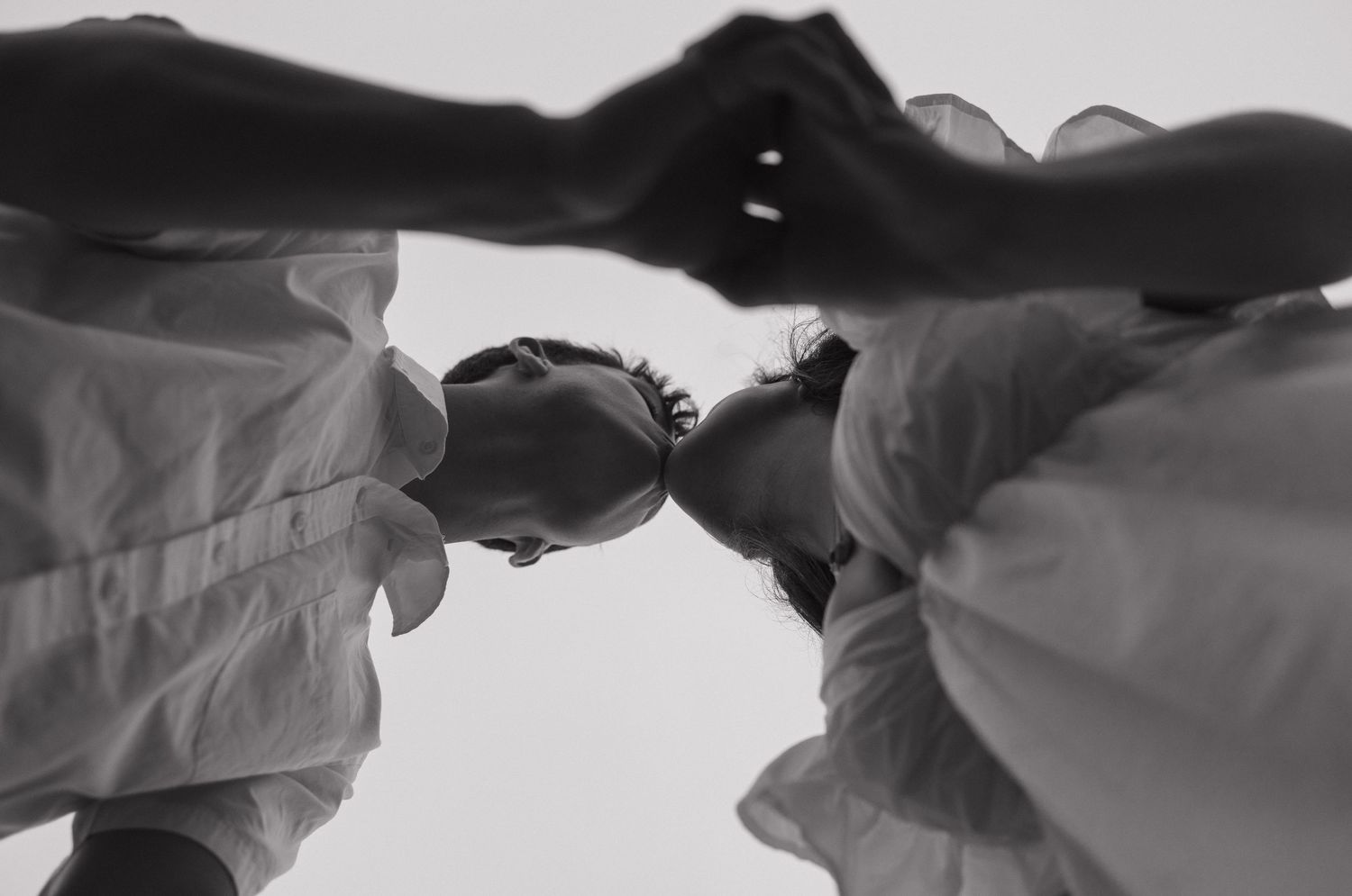 Black and white silhouettes of hands reaching toward each other against a bright background.