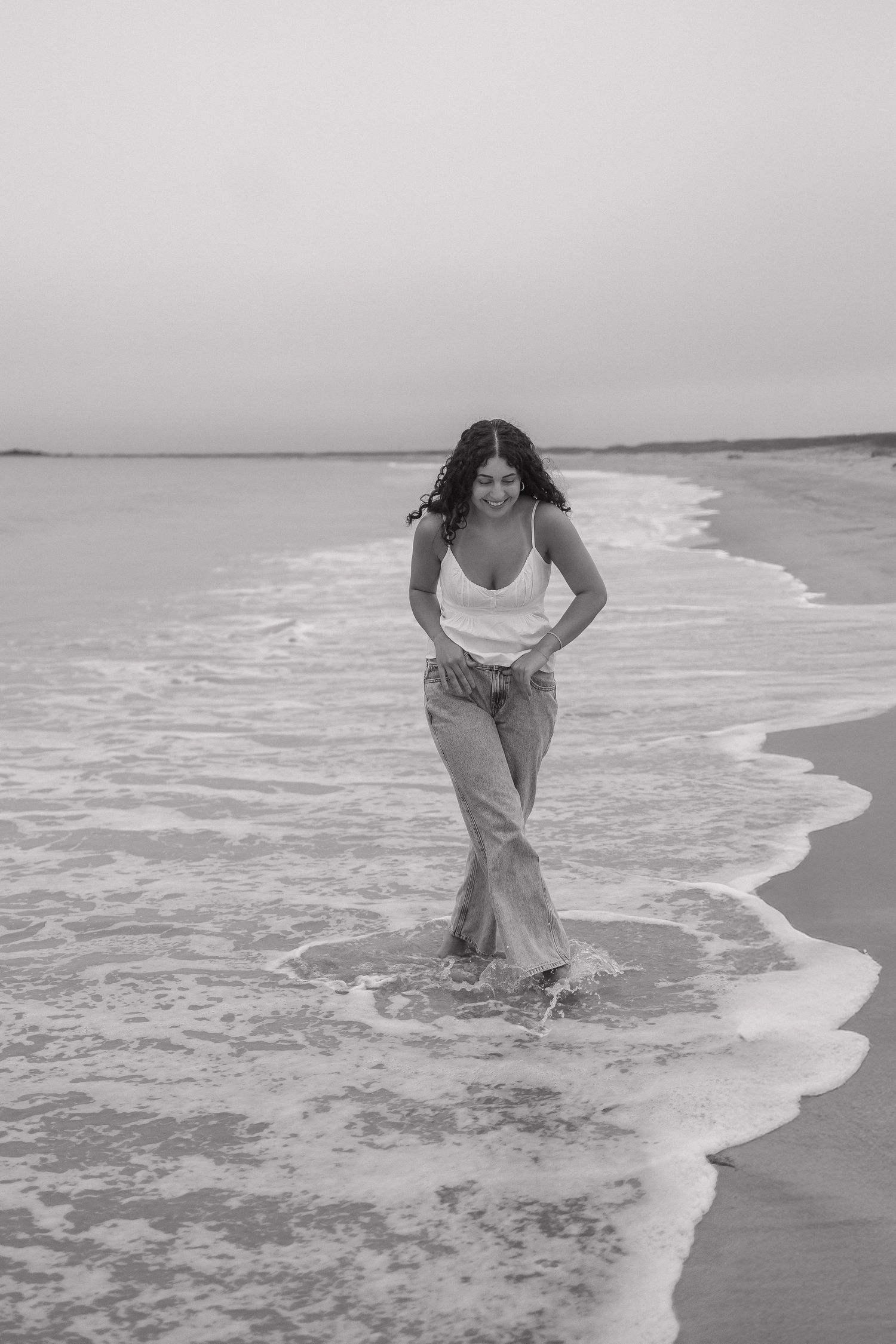 Black and white photo series showing a figure wading into ocean waves at the shoreline on a beach.