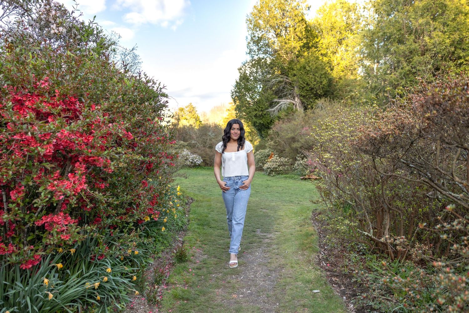 Spring Senior session walking along a lush garden path lined with colorful flowering shrubs. At Kinney Azalea Gardens in Kingston RI