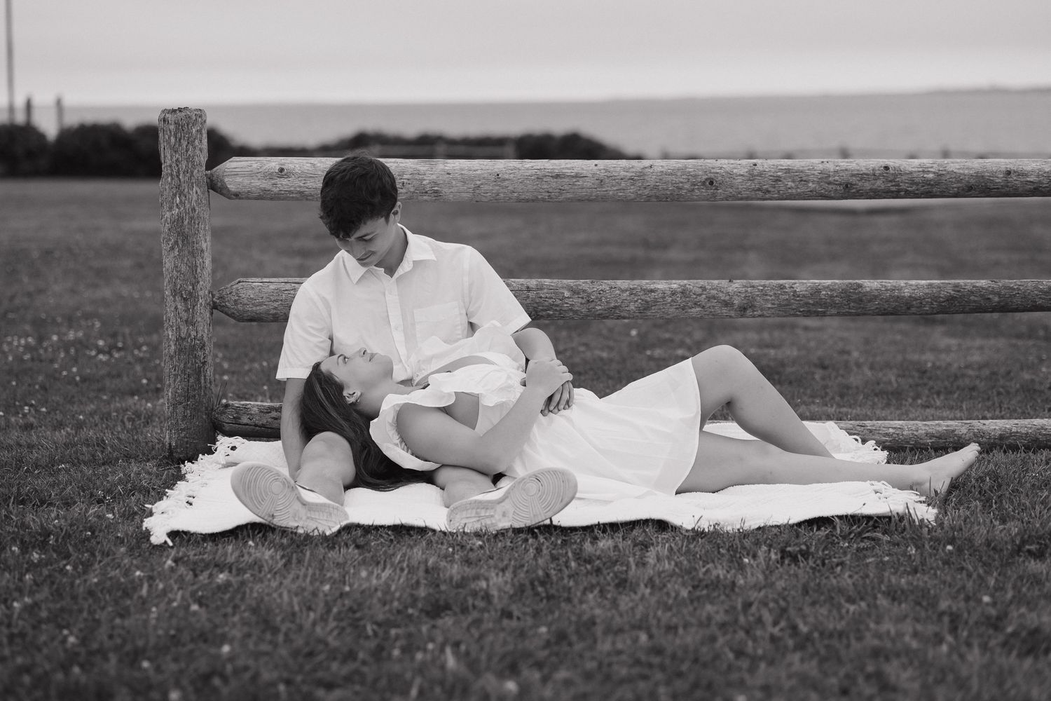 A person in white clothing lies relaxing on a blanket in a grassy field on a sunny day.