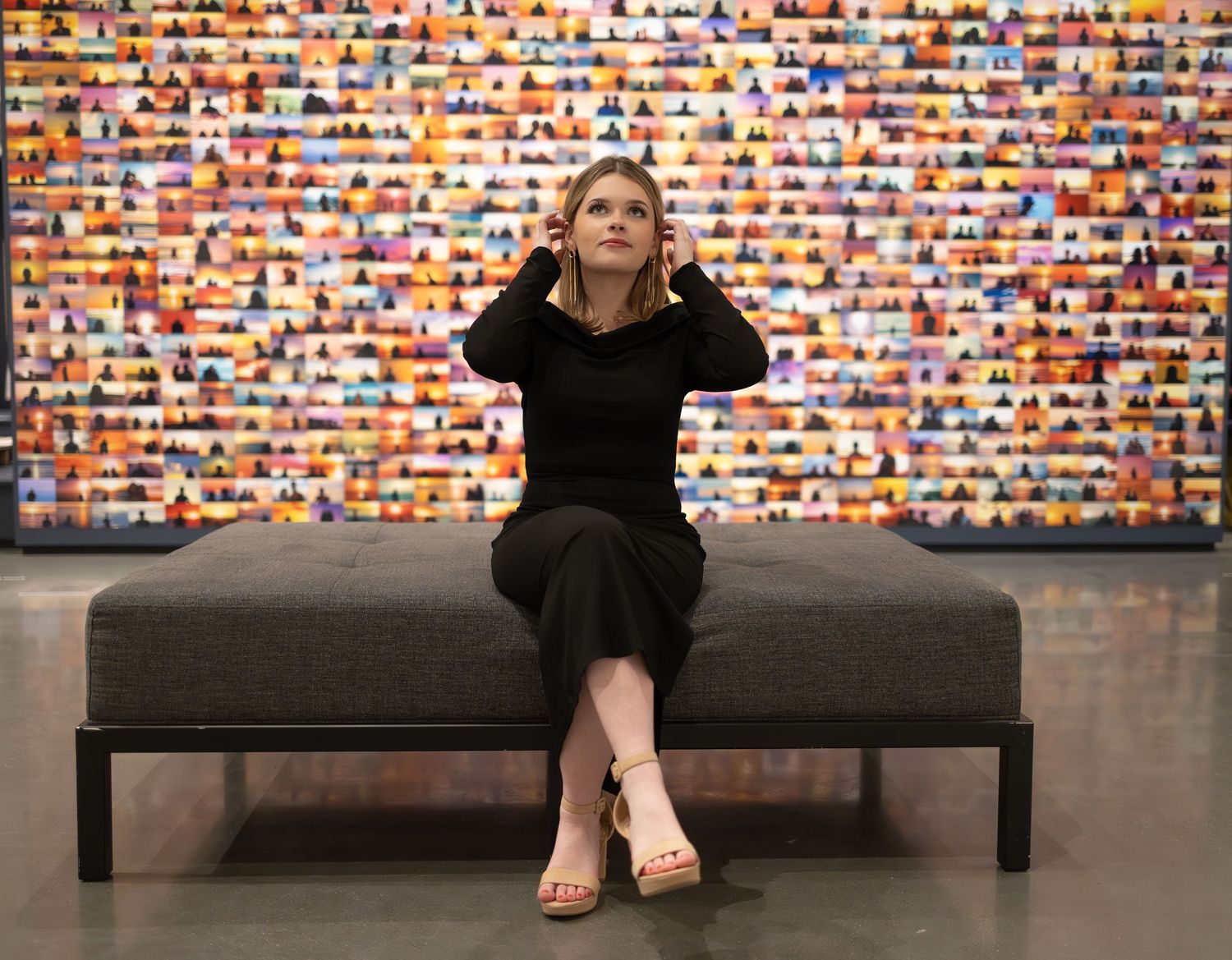 Woman in black dress sits on bench against colorful mosaic wall display in art gallery.