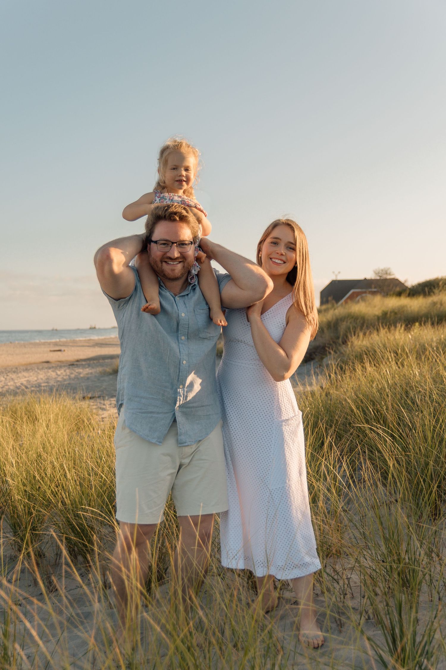 A family shares a joyful moment together on a beach with dunes in the background at golden hour.