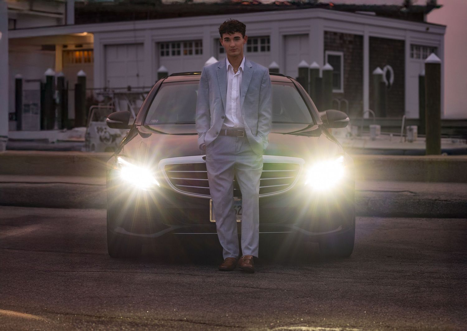 Evening portrait in front of car with headlights on, wearing light colored suit.