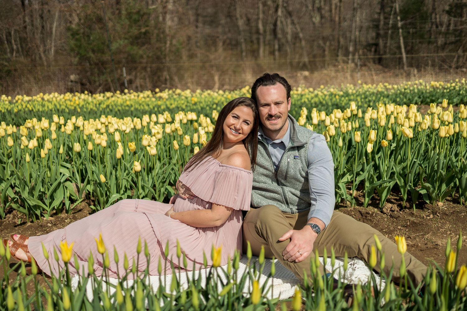 Couple sitting together in field of yellow tulips during springtime photo session.
