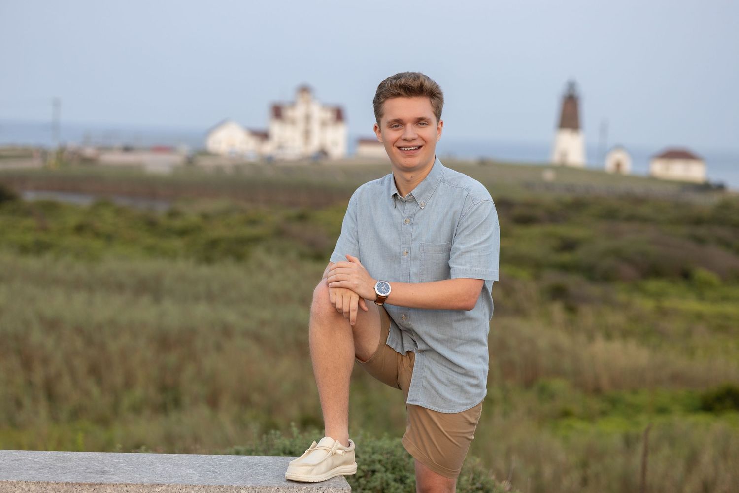 A casual outdoor pose with a lighthouse visible in the distant background.