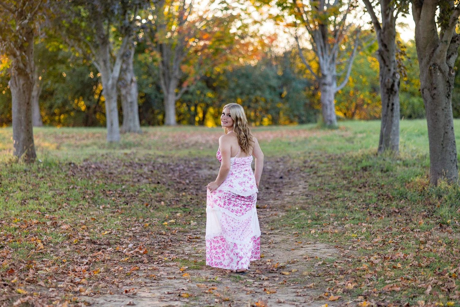 A dreamy scene of someone in a pink dress walking through an autumn grove at sunset.