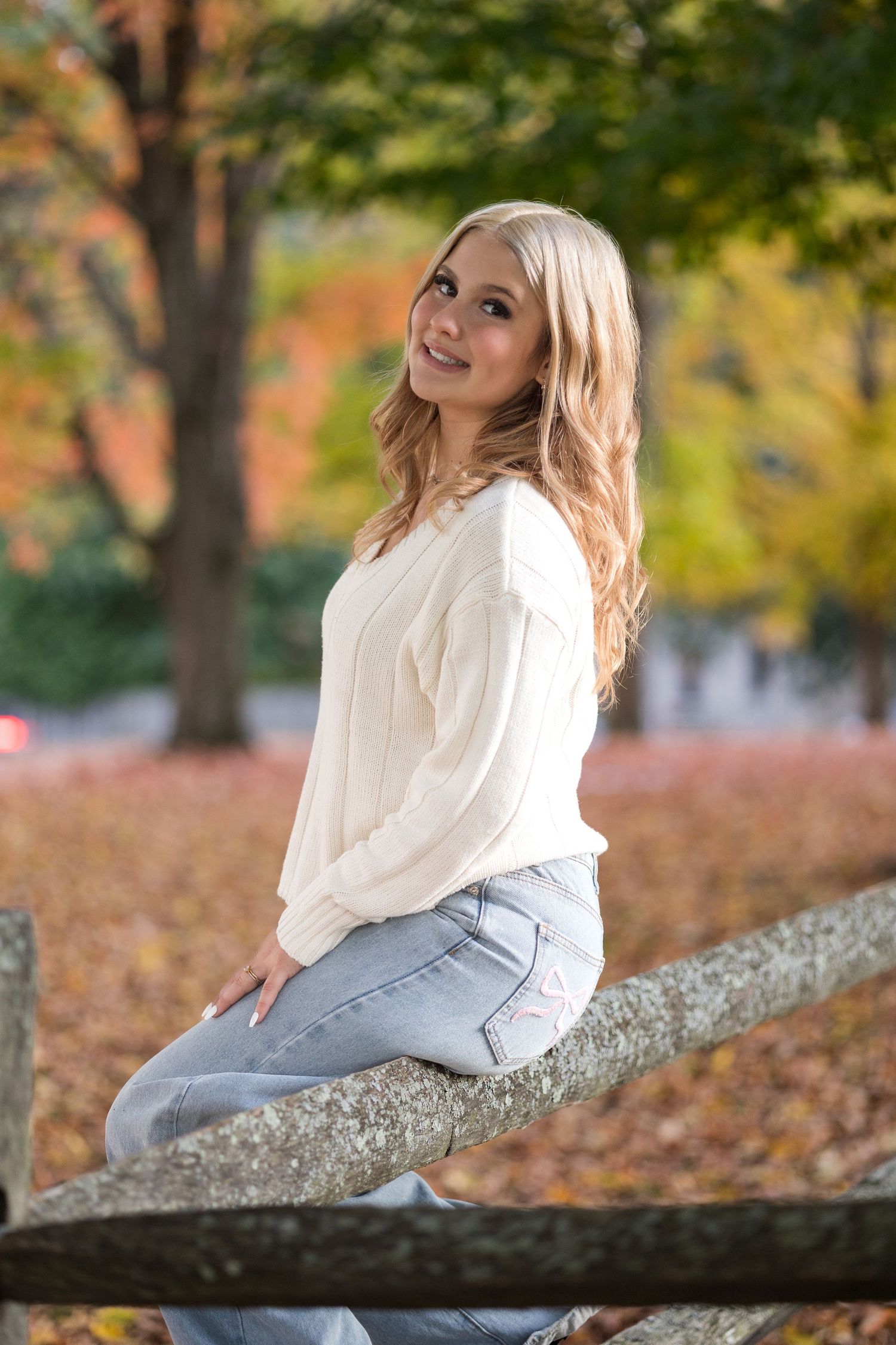 Autumn portrait session on a fallen tree branch with colorful fall foliage in the background.
